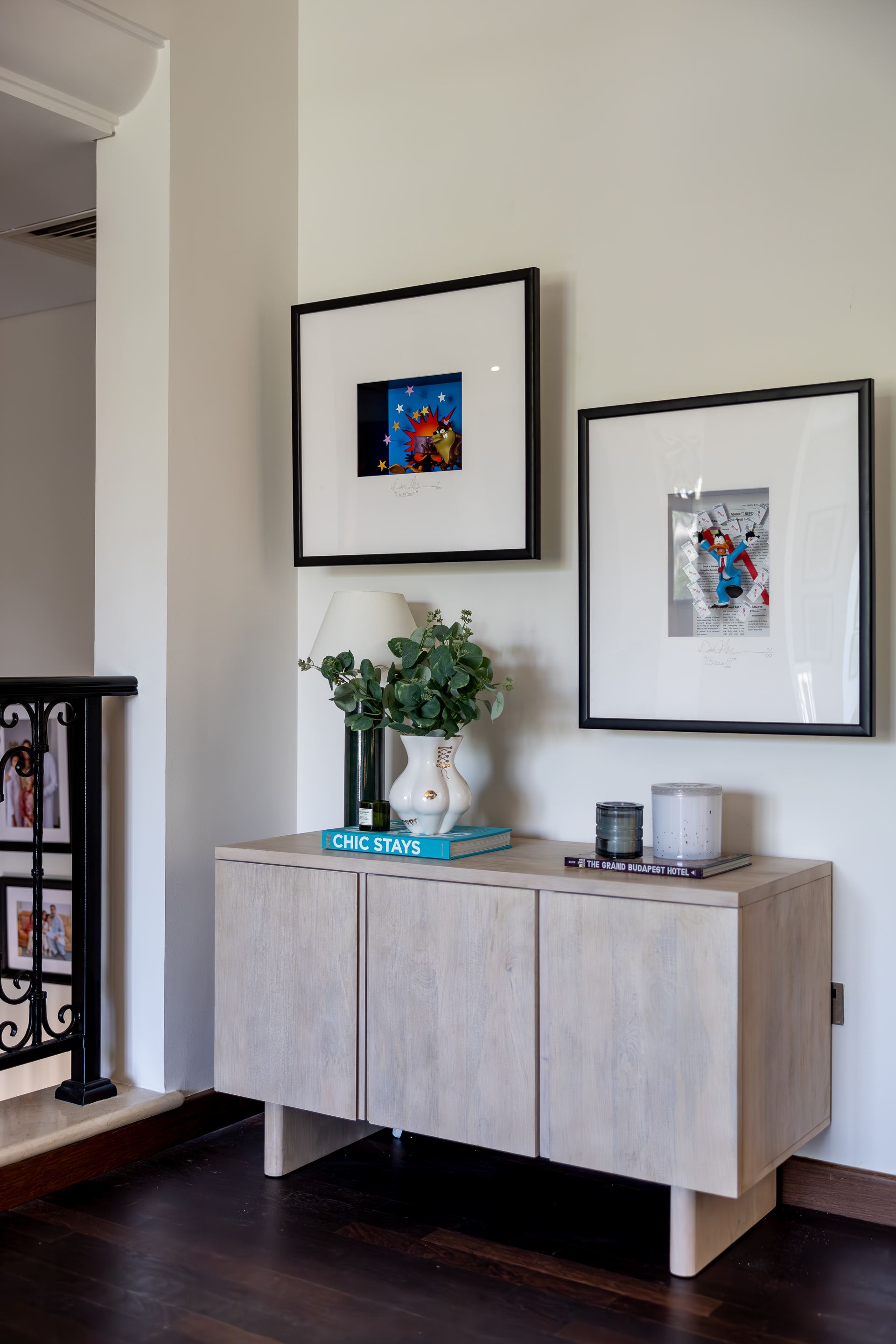 Whitewashed console styled with framed art and eucalyptus beneath a curved pendant light