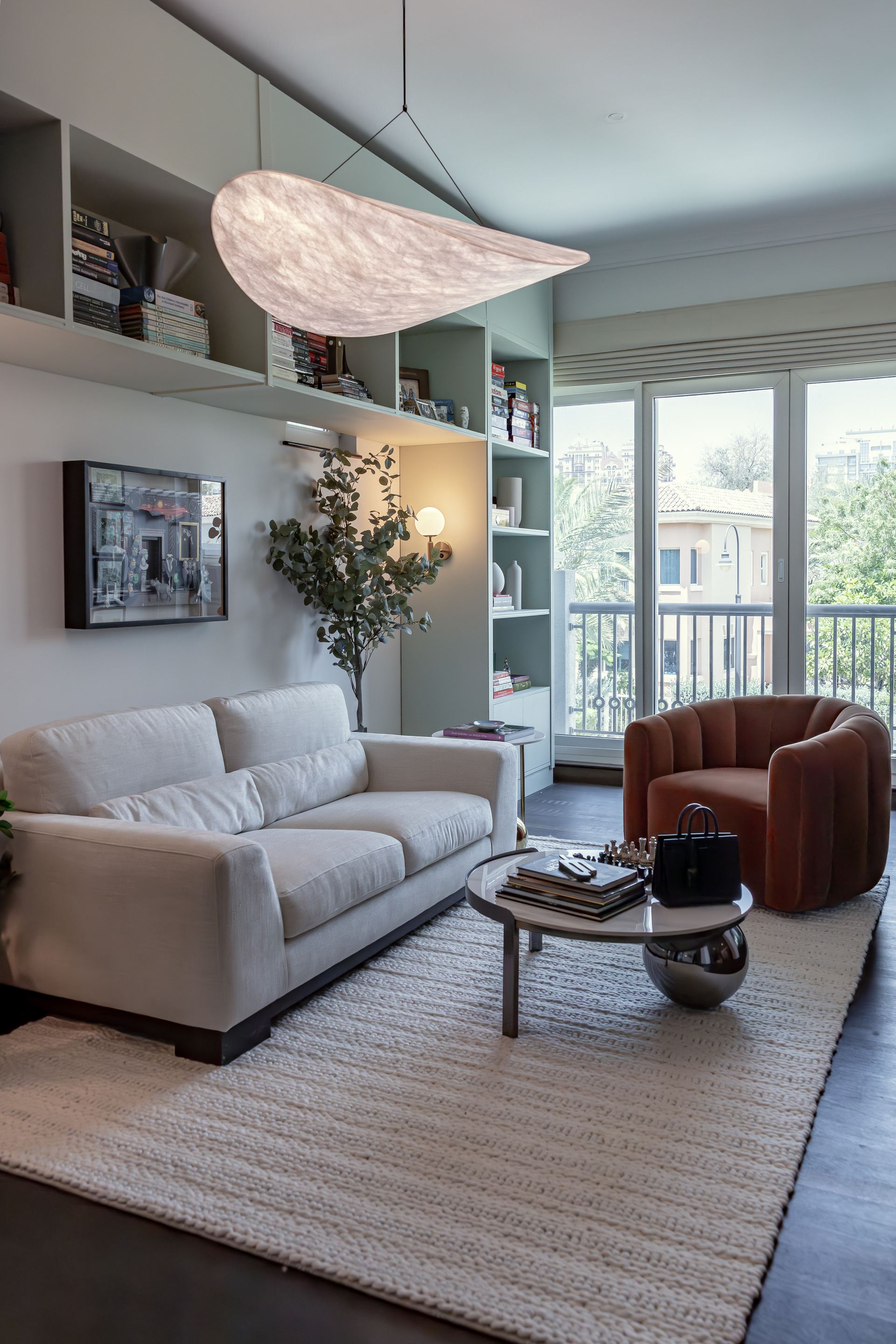 Living room with built-in green shelving, a curved pendant light, and a terracotta armchair