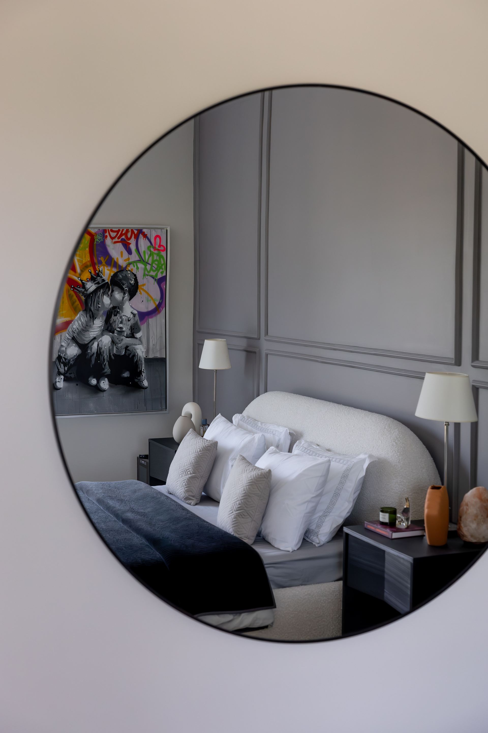 Round mirror reflecting a bedside lamp and graffiti-style portrait painting