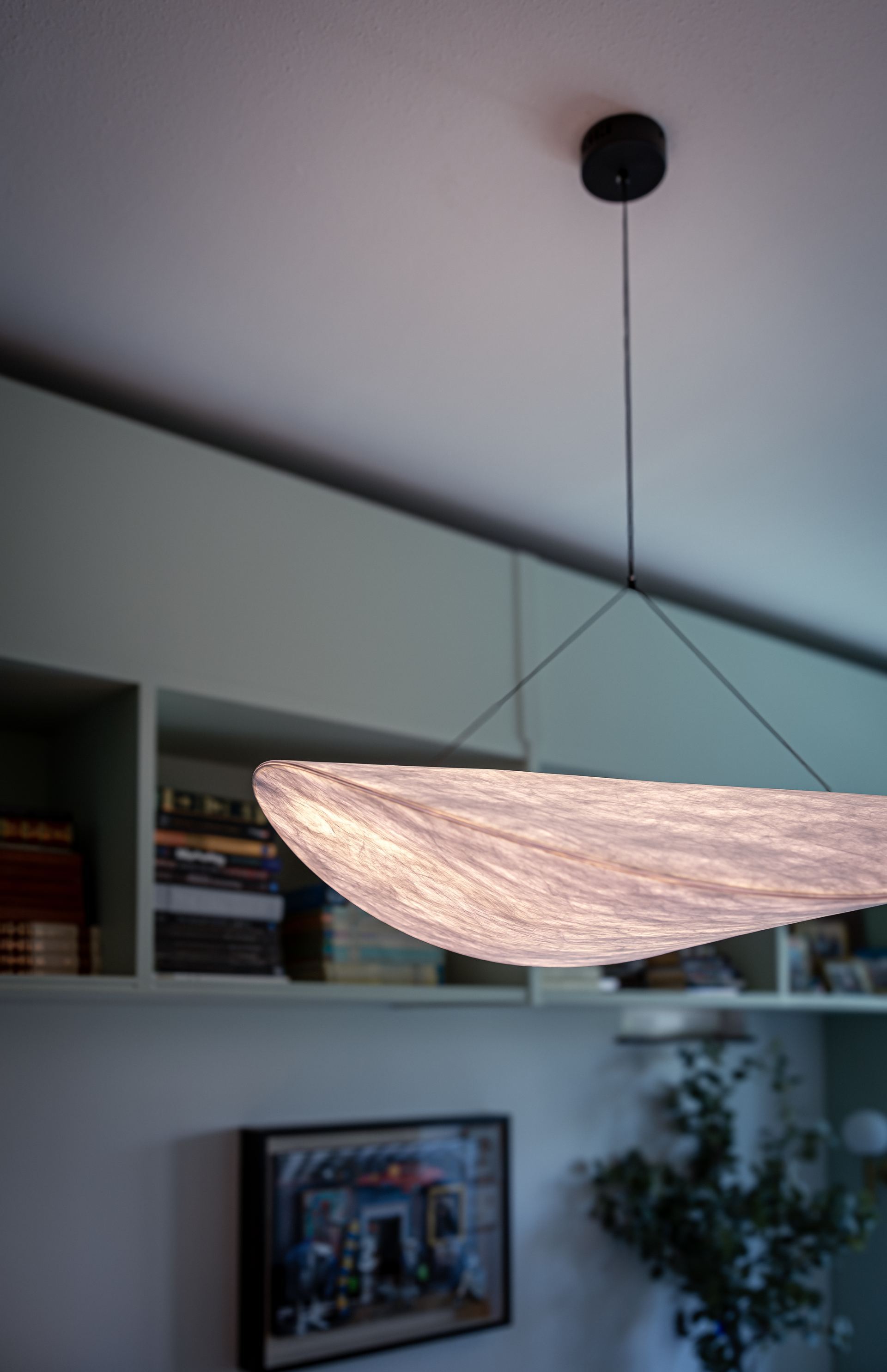 Detail of a woven cocoon pendant light against built-in green shelving