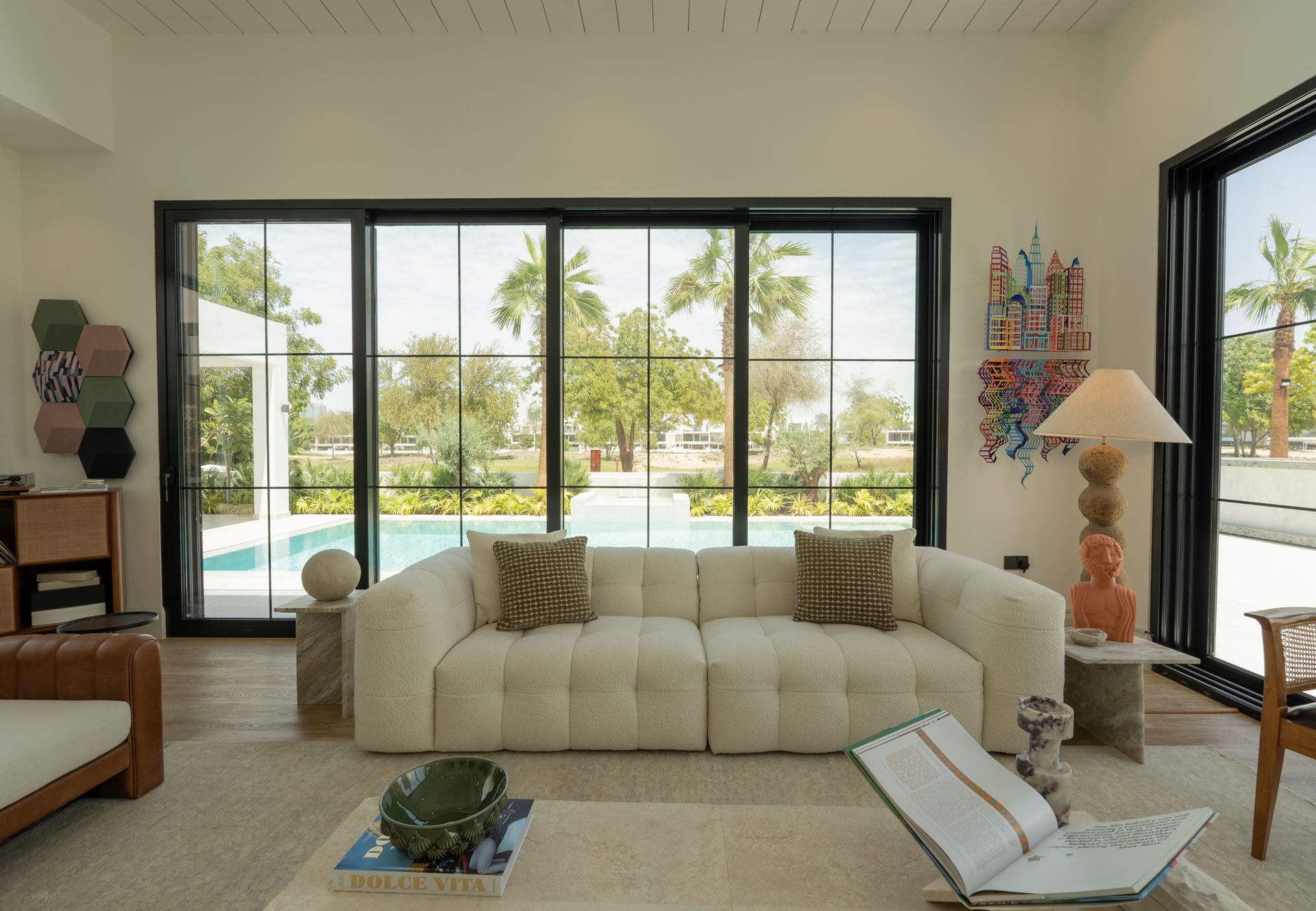 Cream sectional sofa facing floor-to-ceiling windows overlooking the pool and palms