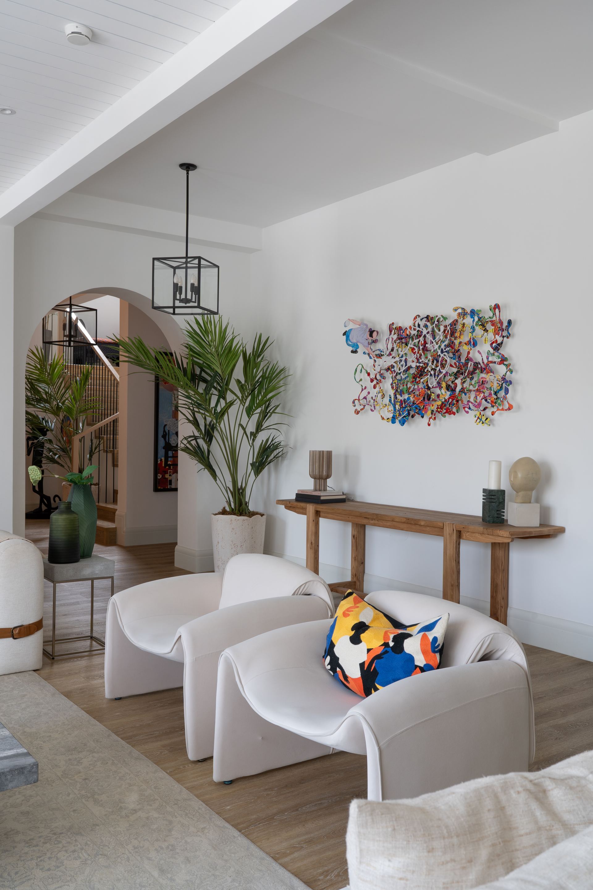 Curved bouclé armchairs beside a walnut console with a colorful cushion