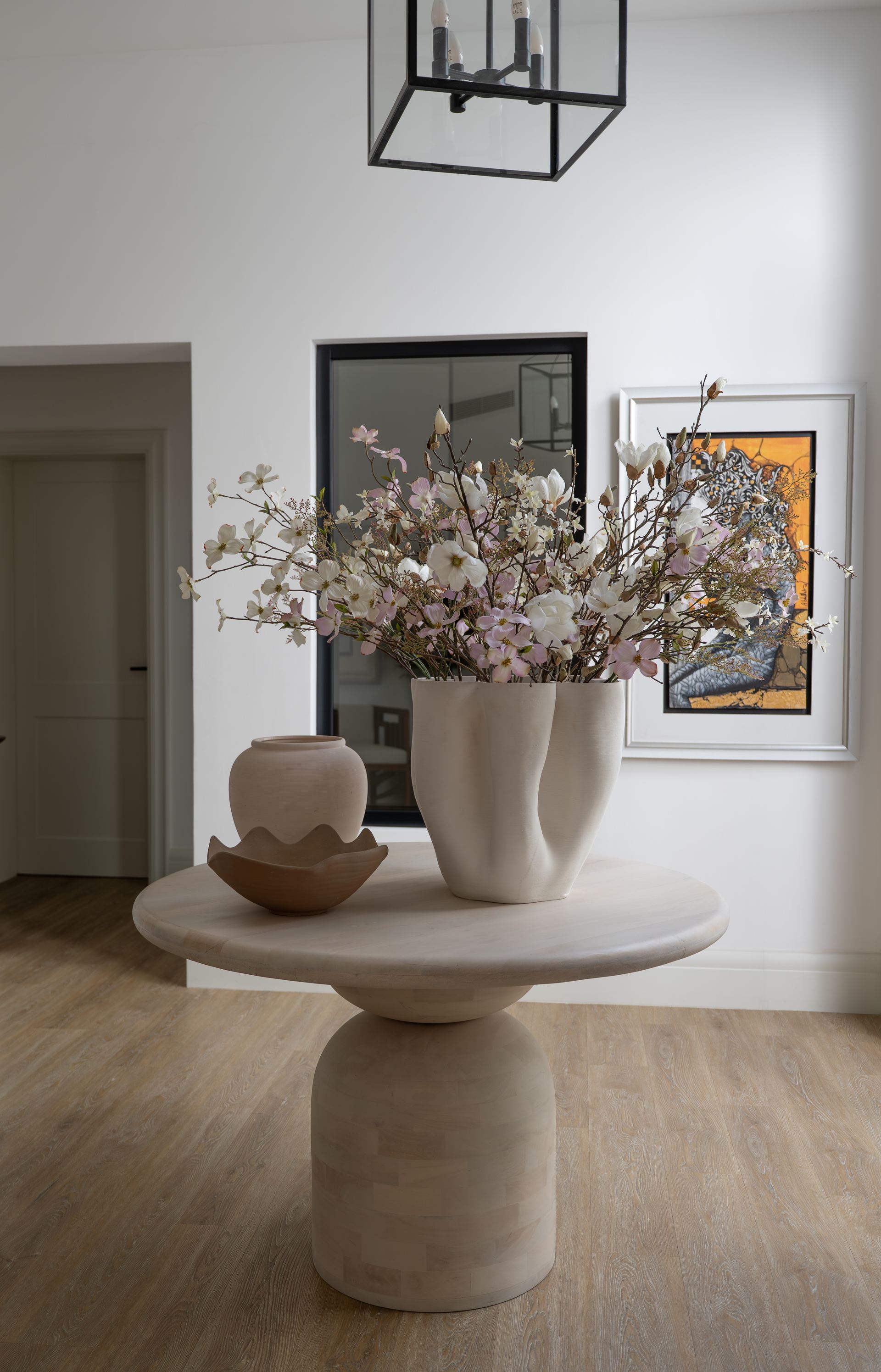 Sculptural ceramic vase filled with white blossoms on a pedestal side table