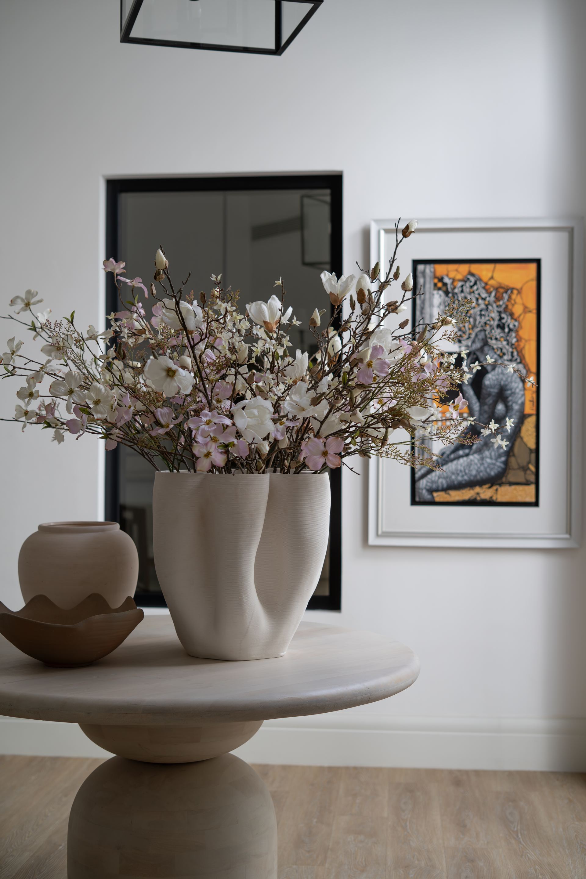 Sculptural ceramic vase of white blossoms beside a framed figurative painting
