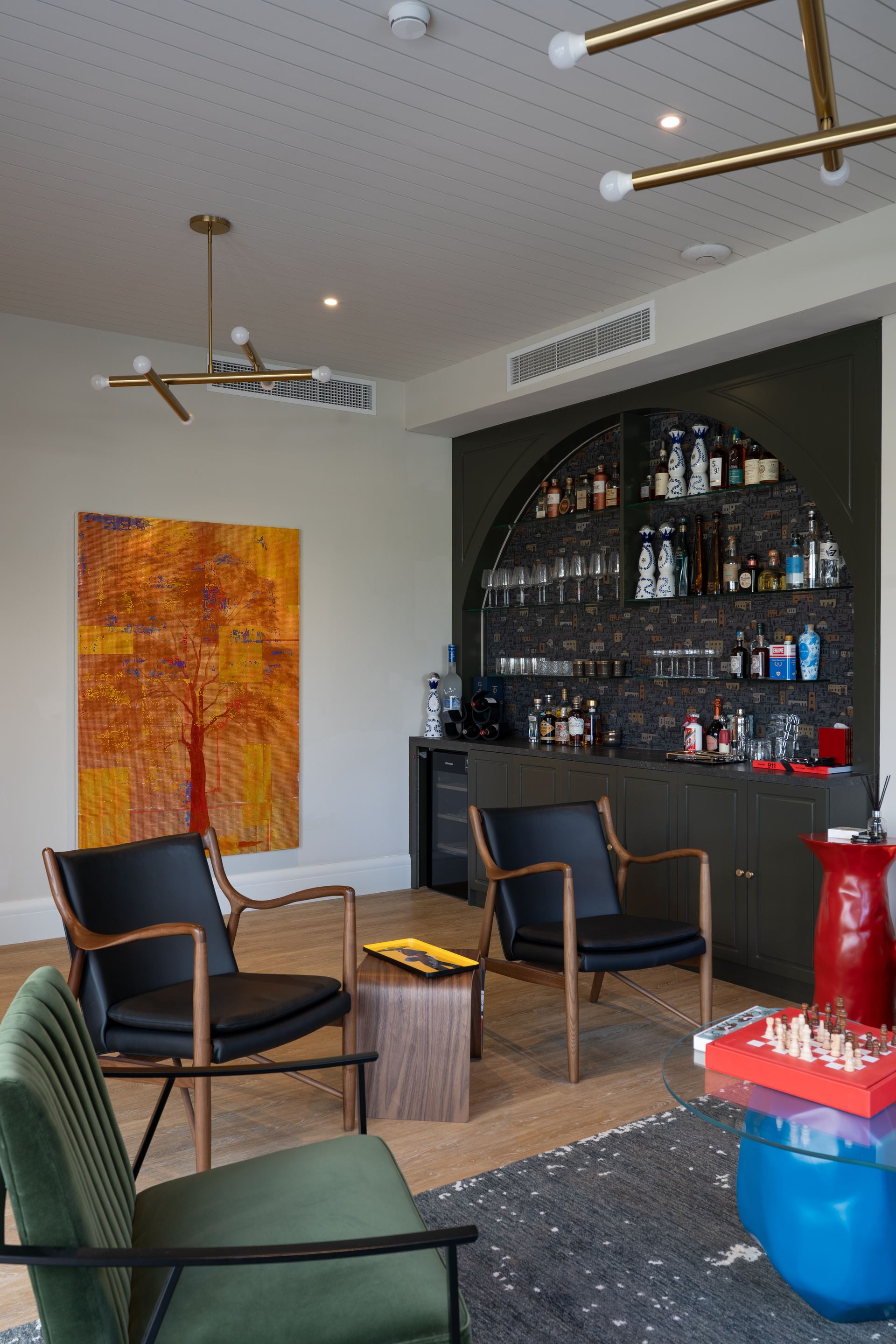 Home bar with a curved arched shelf, leather campaign chairs, and brass pendant lights