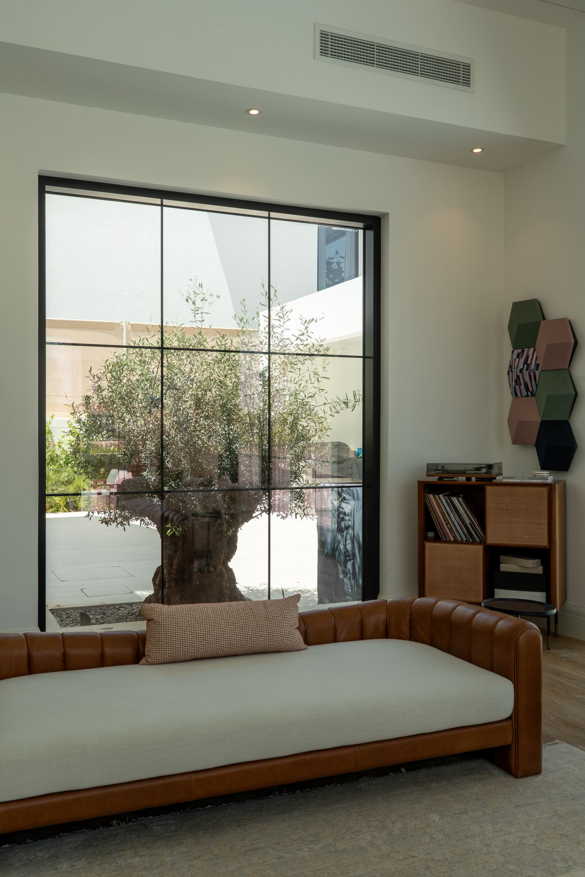 Leather Chesterfield-style daybed facing a courtyard olive tree through glazed doors