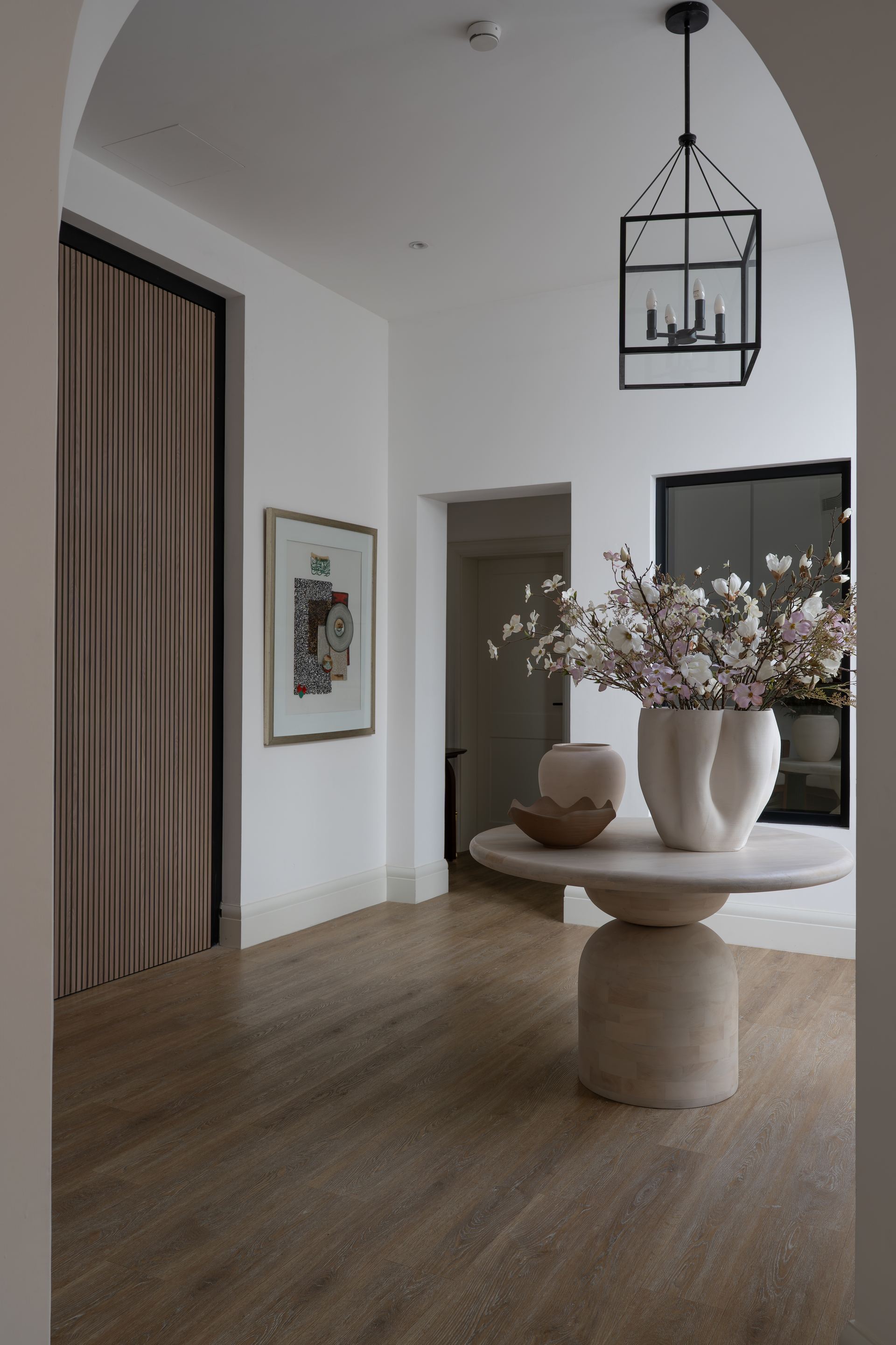 Sculptural travertine console table with a ceramic vase beneath a black lantern pendant