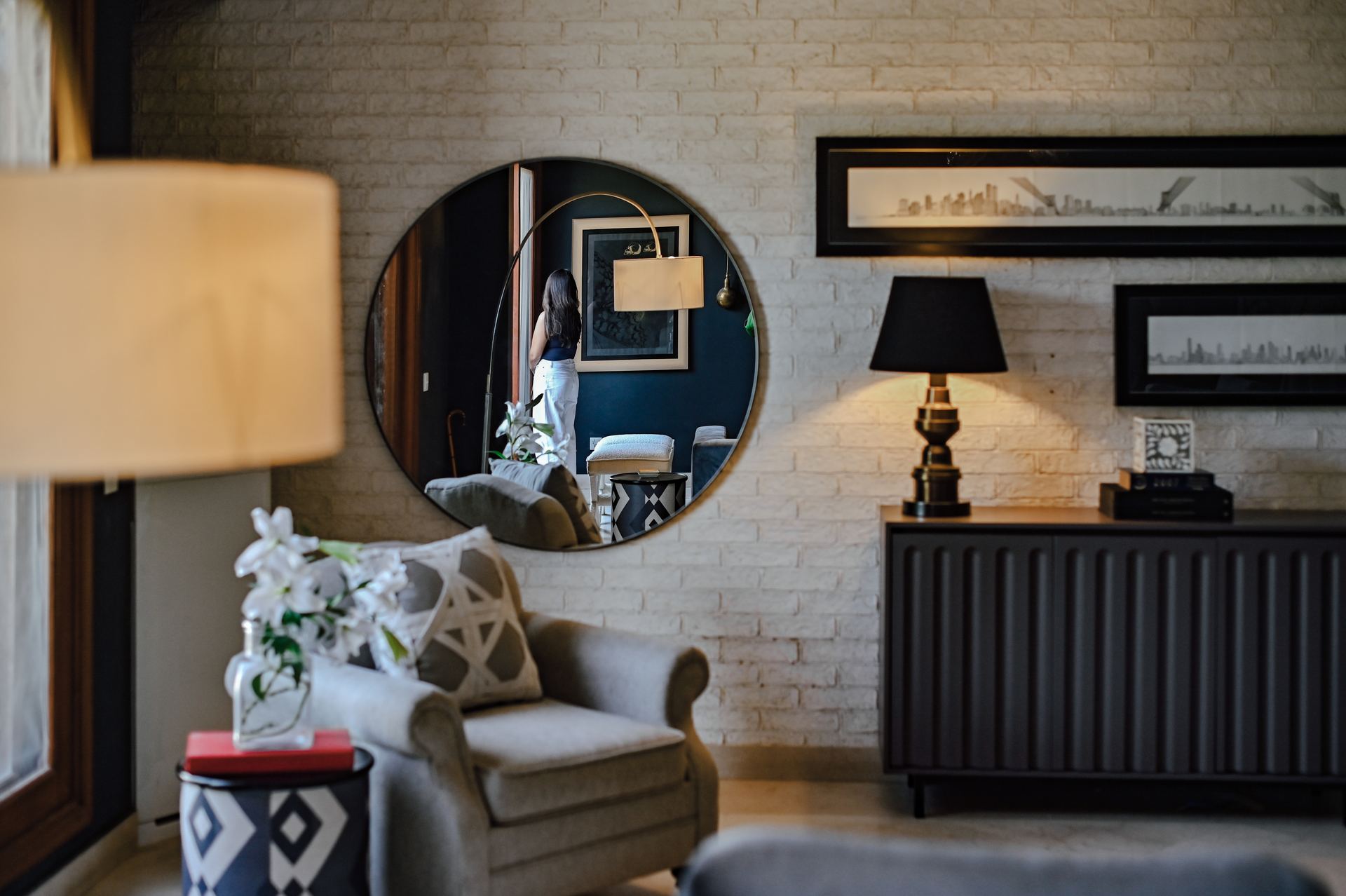 Round mirror reflecting an arc floor lamp beside a charcoal brick wall