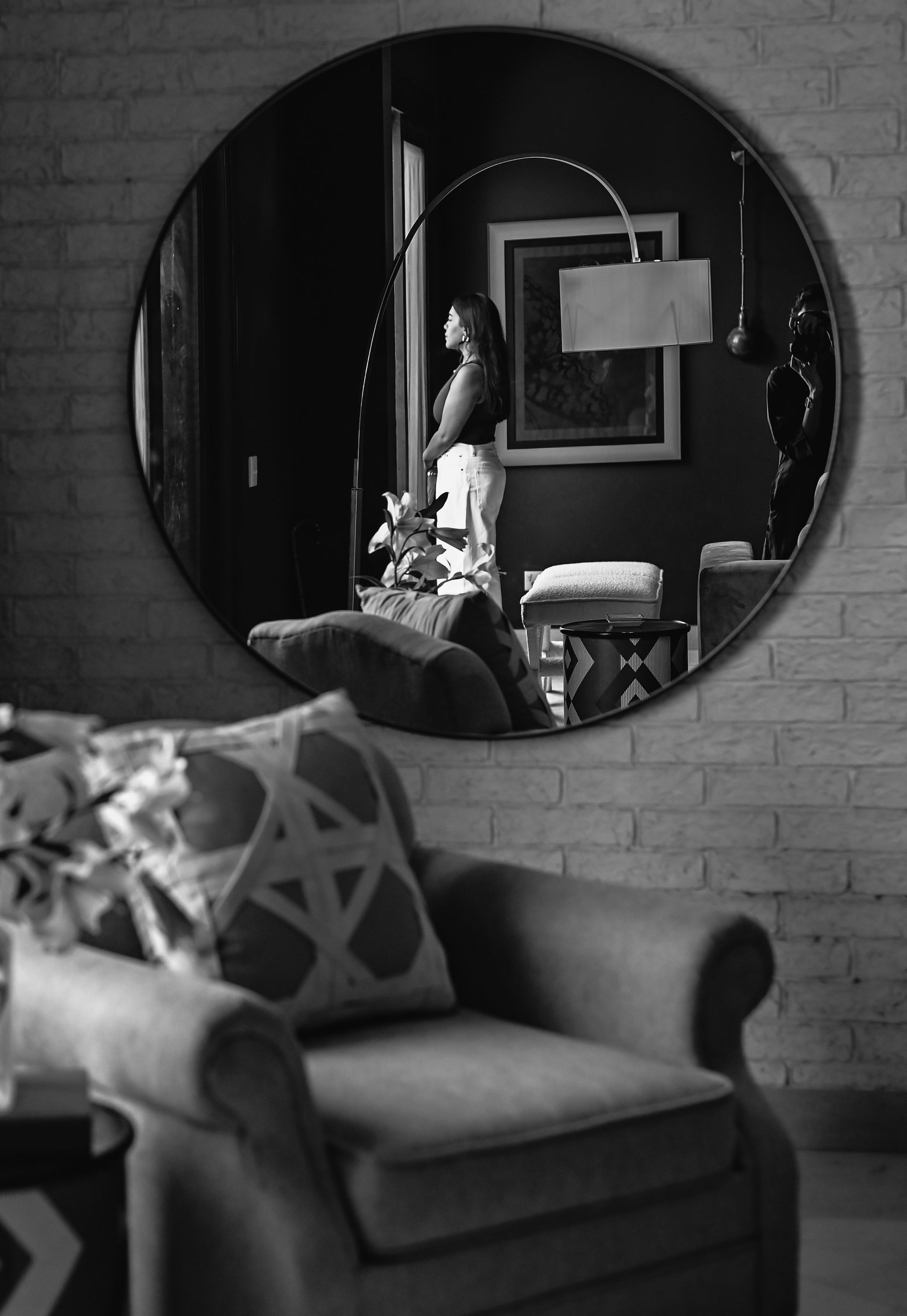 Round mirror reflecting an arc floor lamp beside a black cabinet