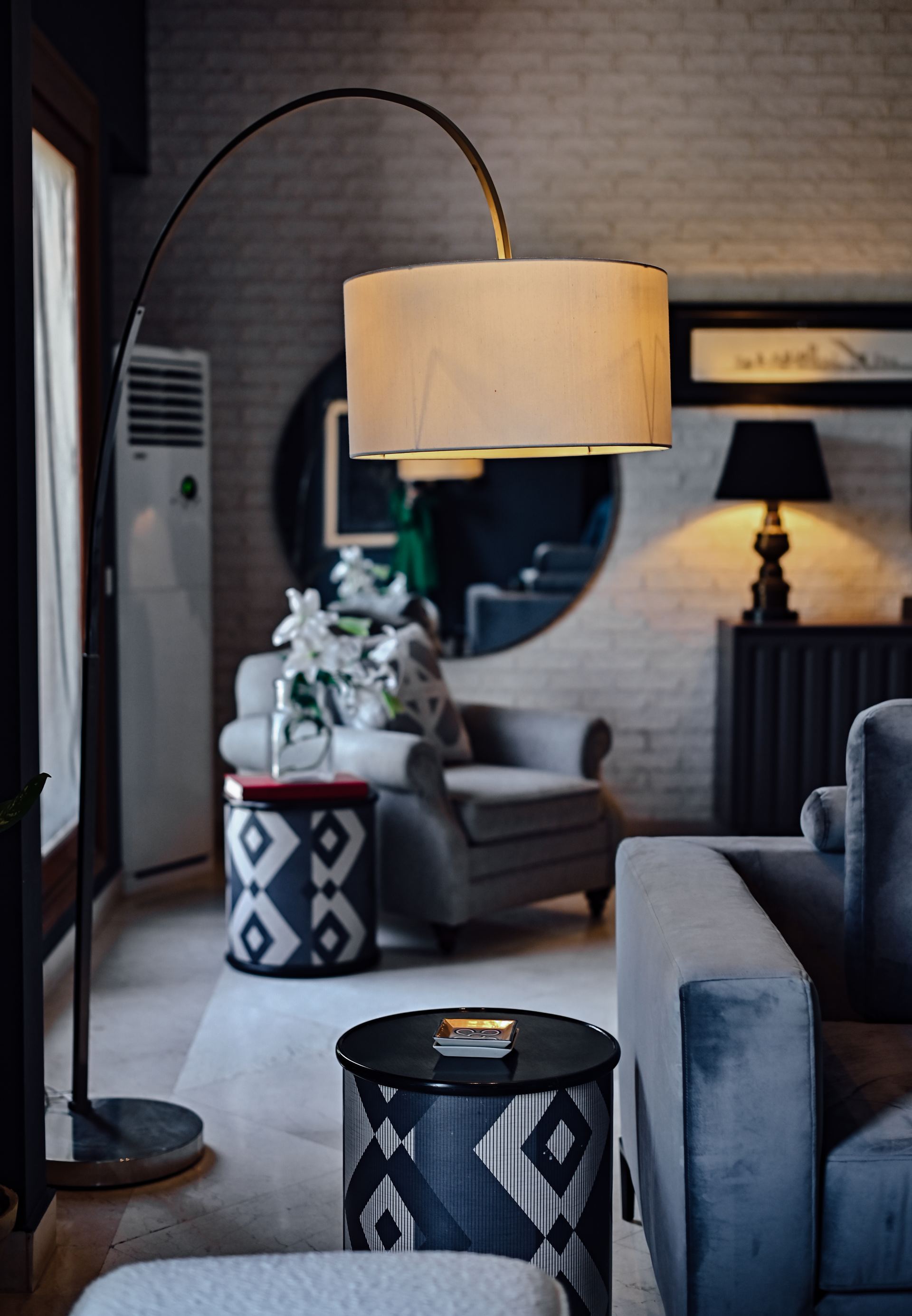 Curved brass floor lamp with a linen shade above patterned Moroccan side tables