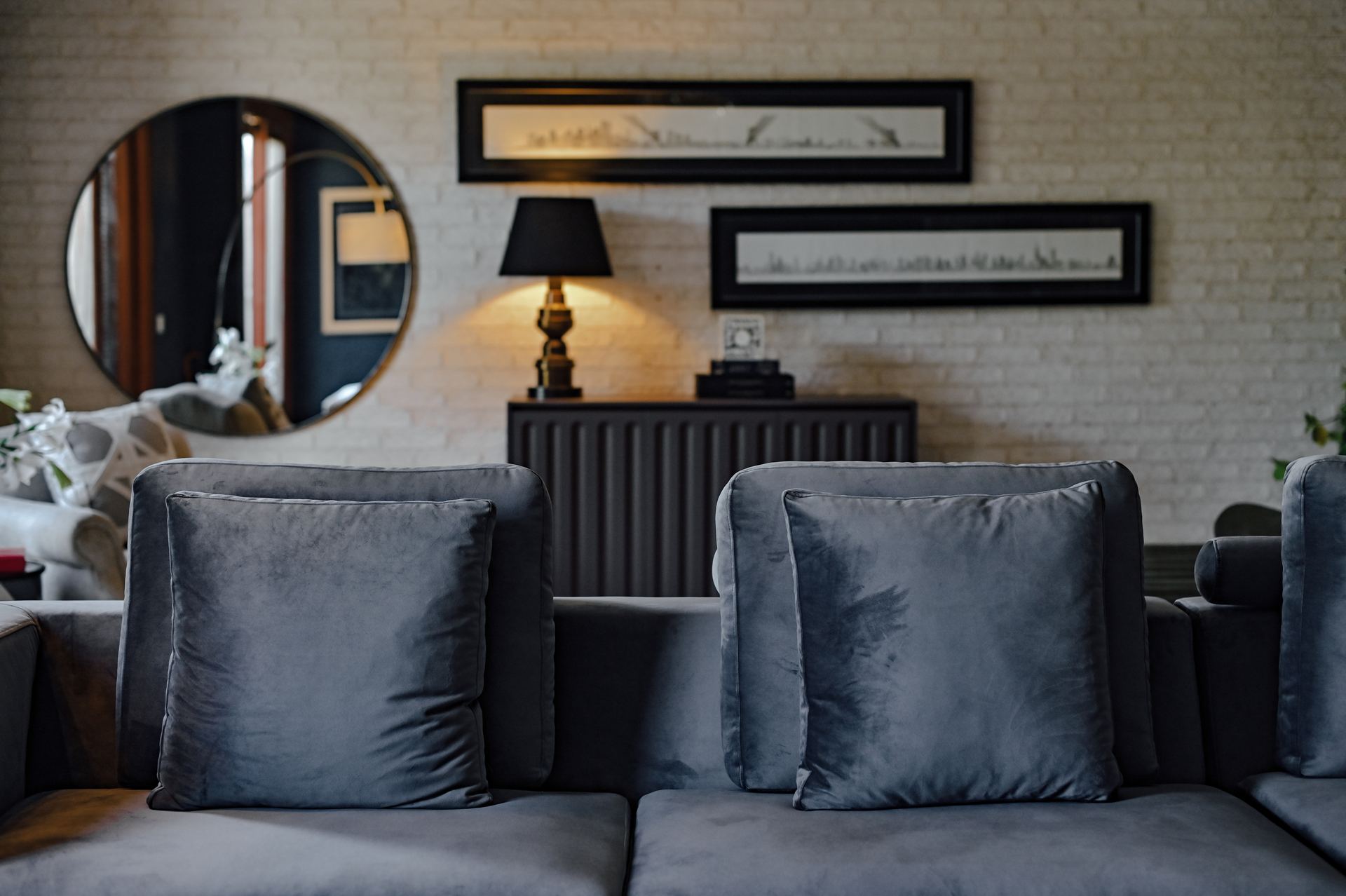 Charcoal velvet cushions in front of a brass table lamp and framed skyline art