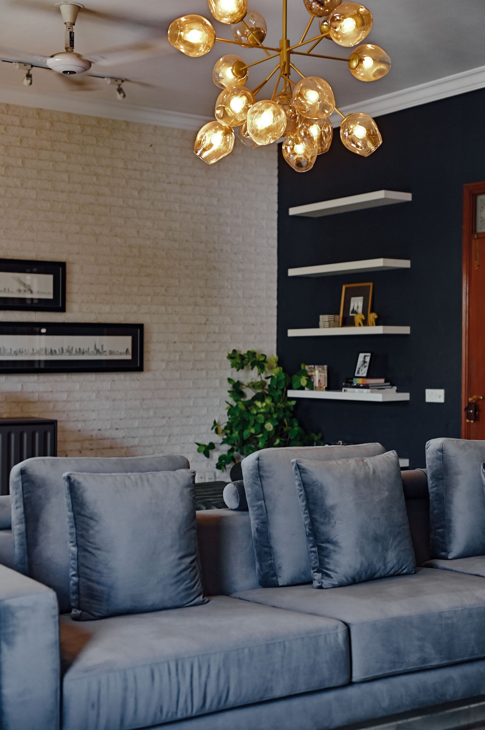 Brass sputnik chandelier above a grey sofa with built-in shelving on a navy wall
