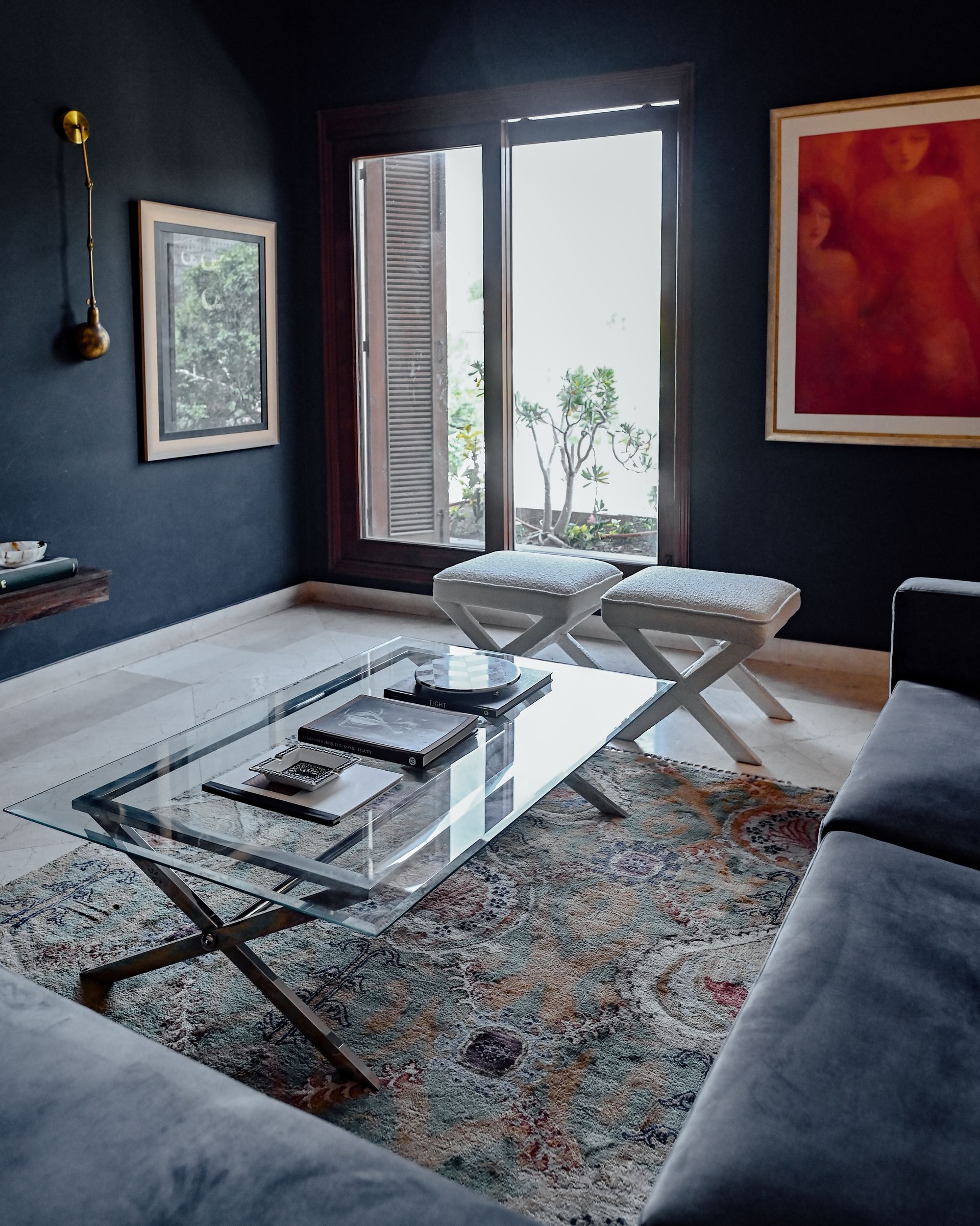 Glass coffee table with X-frame stools beside a brass wall sconce