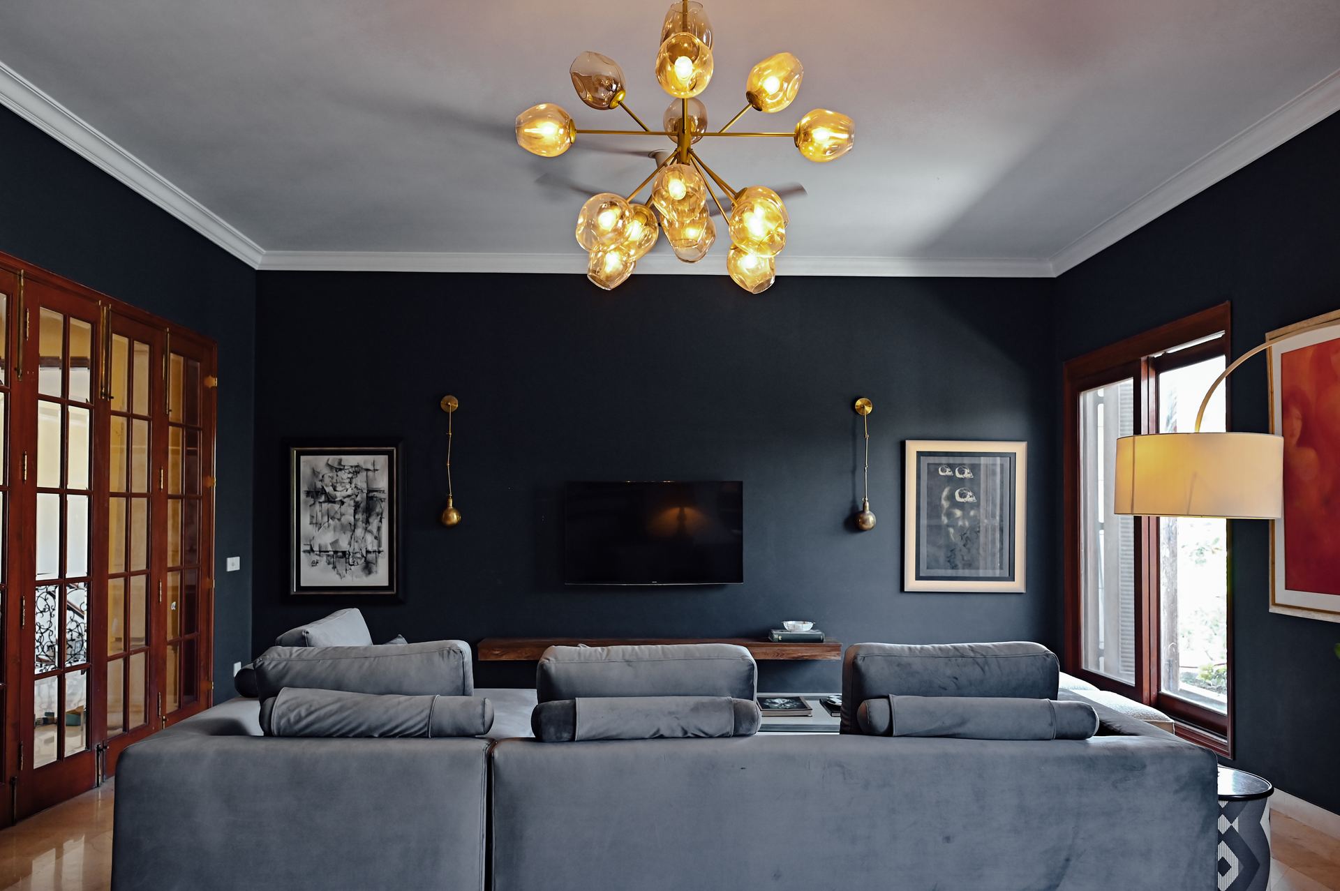 Grey sectional sofa facing a wall-mounted TV beneath a brass sputnik chandelier