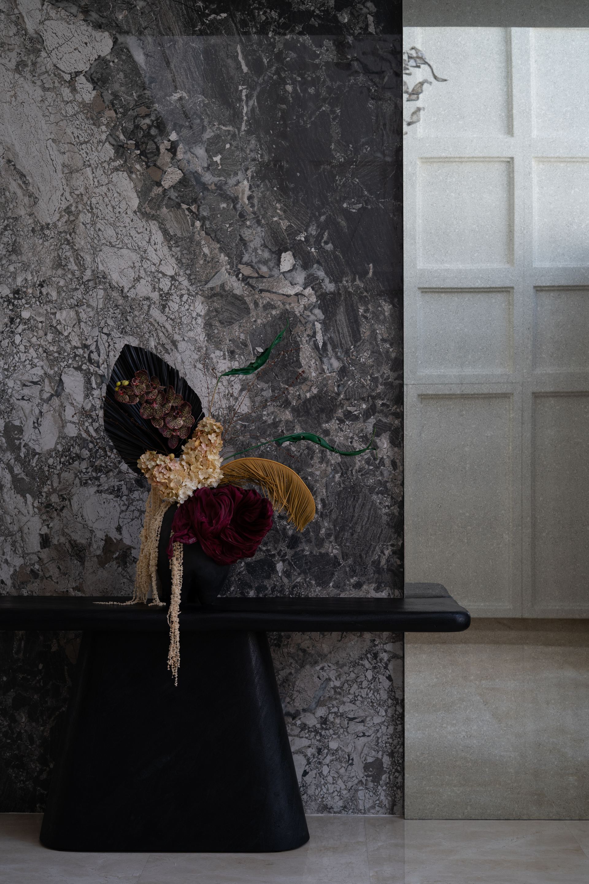 Dried floral arrangement in a dark vessel on a black console against a grey marble wall