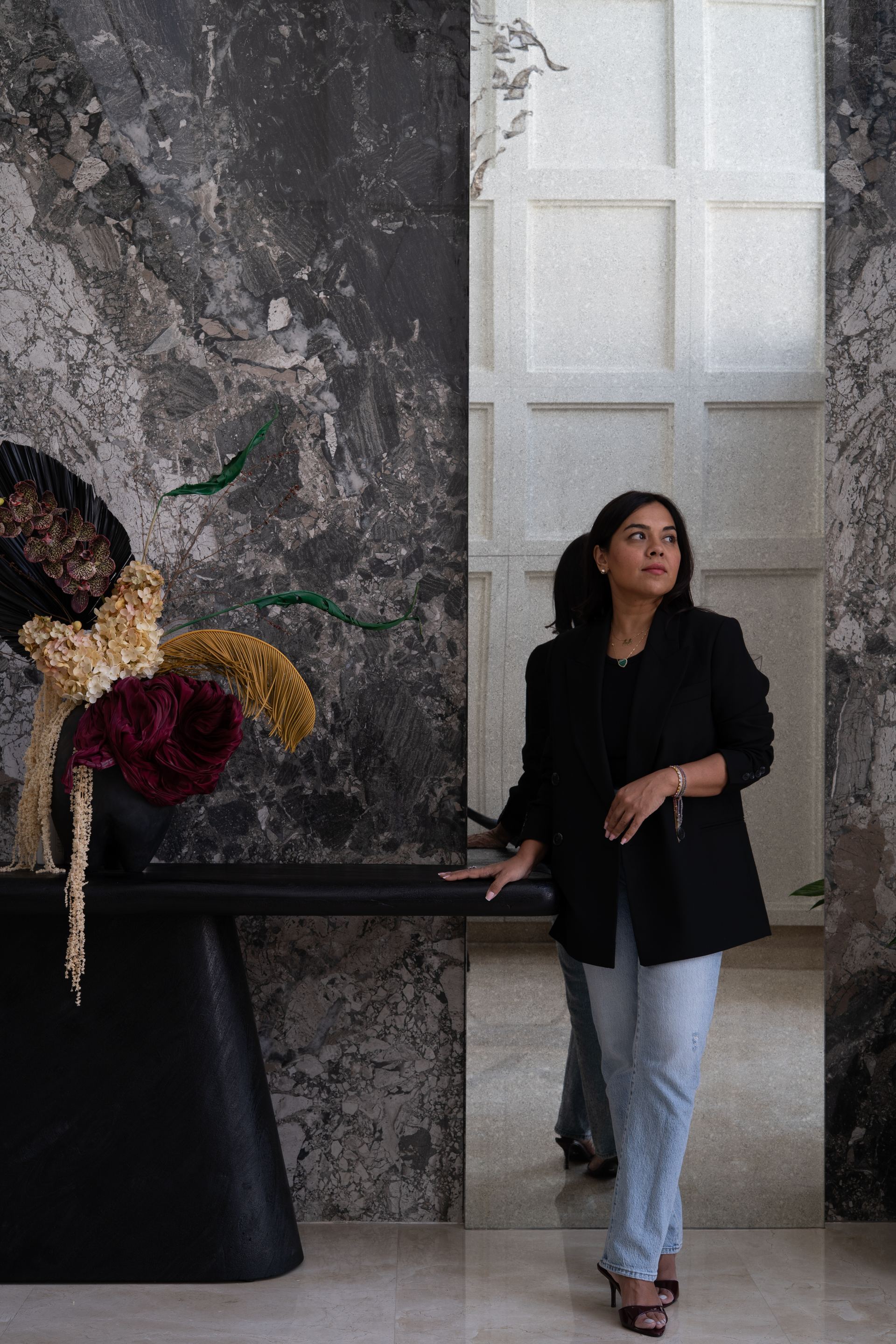 Black console styled with a dried floral arrangement against a stone-grey marble wall