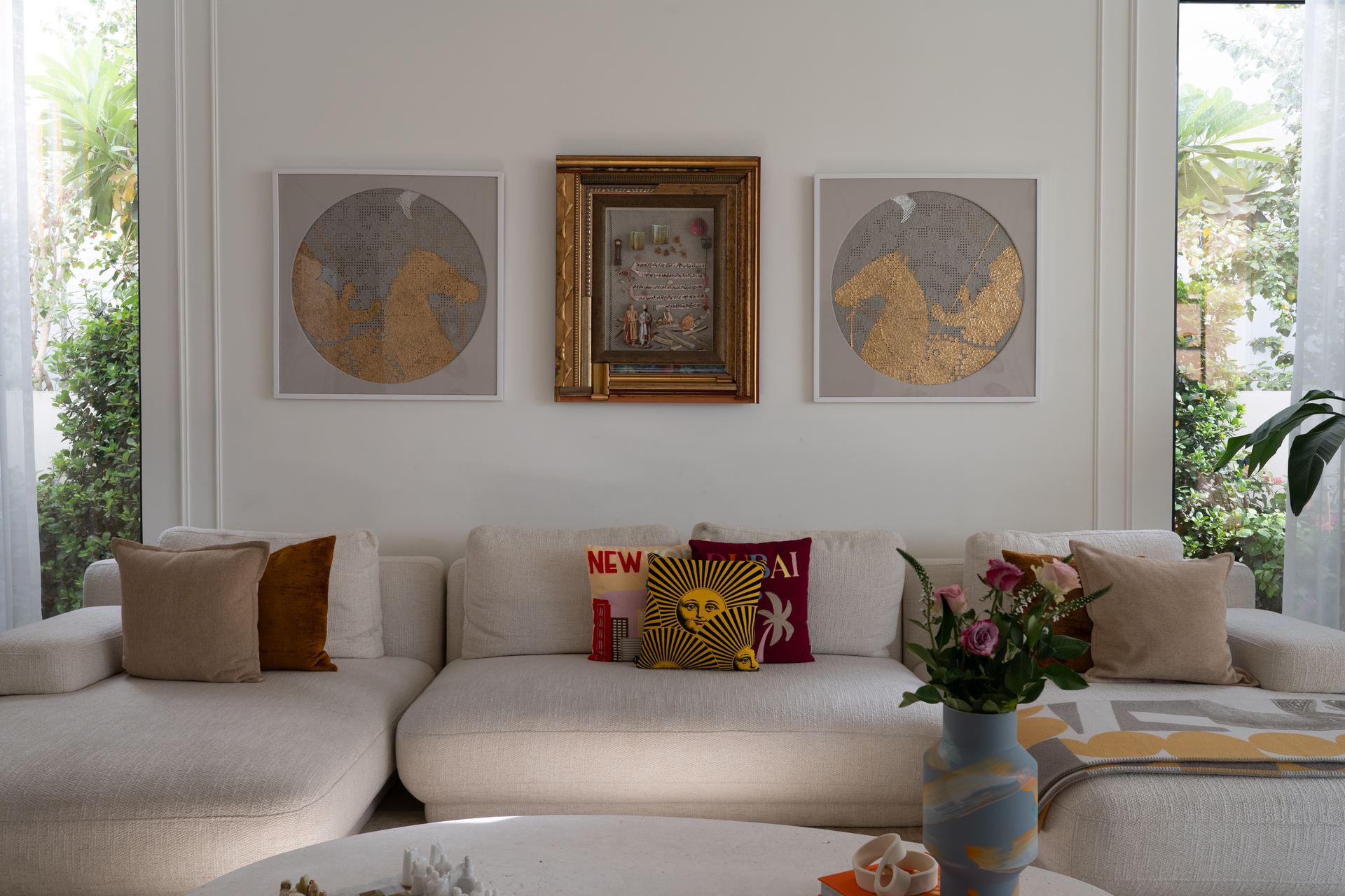 Round gold-leaf artworks flank a framed vintage print above a cream sofa