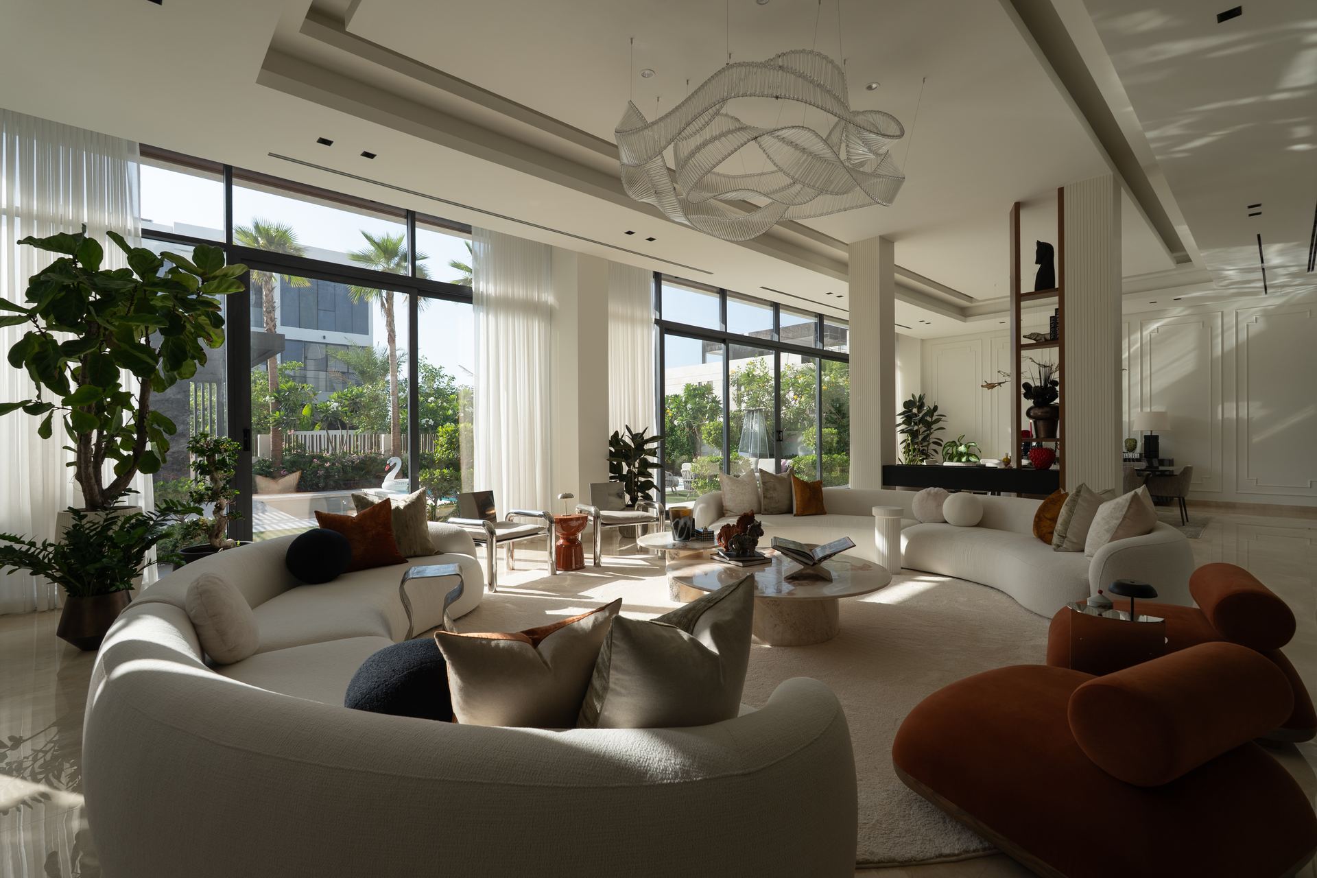 Curved white sofas arranged around a sculptural chandelier in an open-plan living room