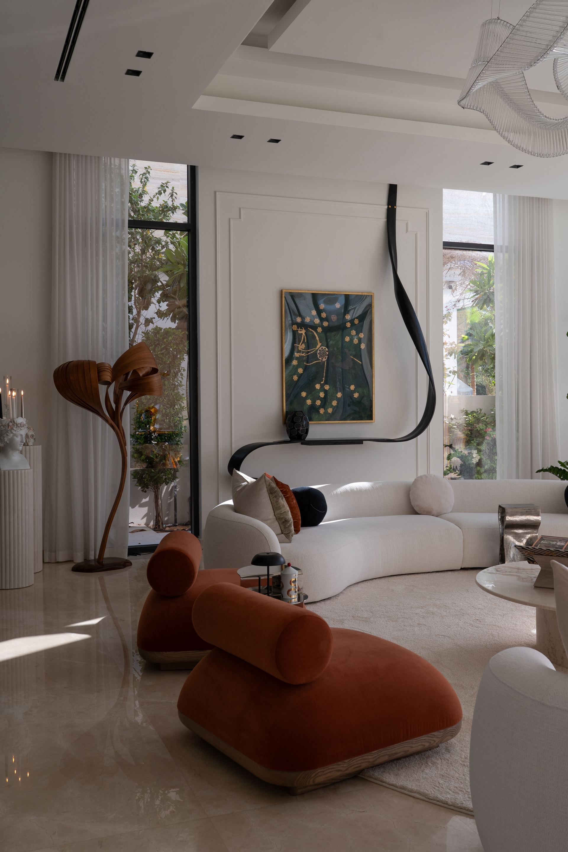 Terracotta bolster chairs beside a curved white sofa and framed botanical painting