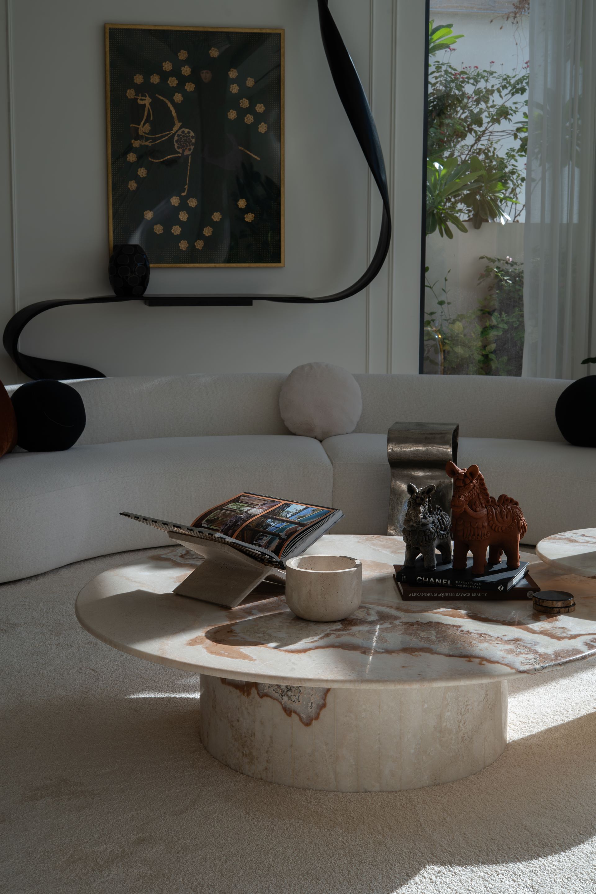 Round travertine coffee table styled with sculptures beneath a sculptural black wall light