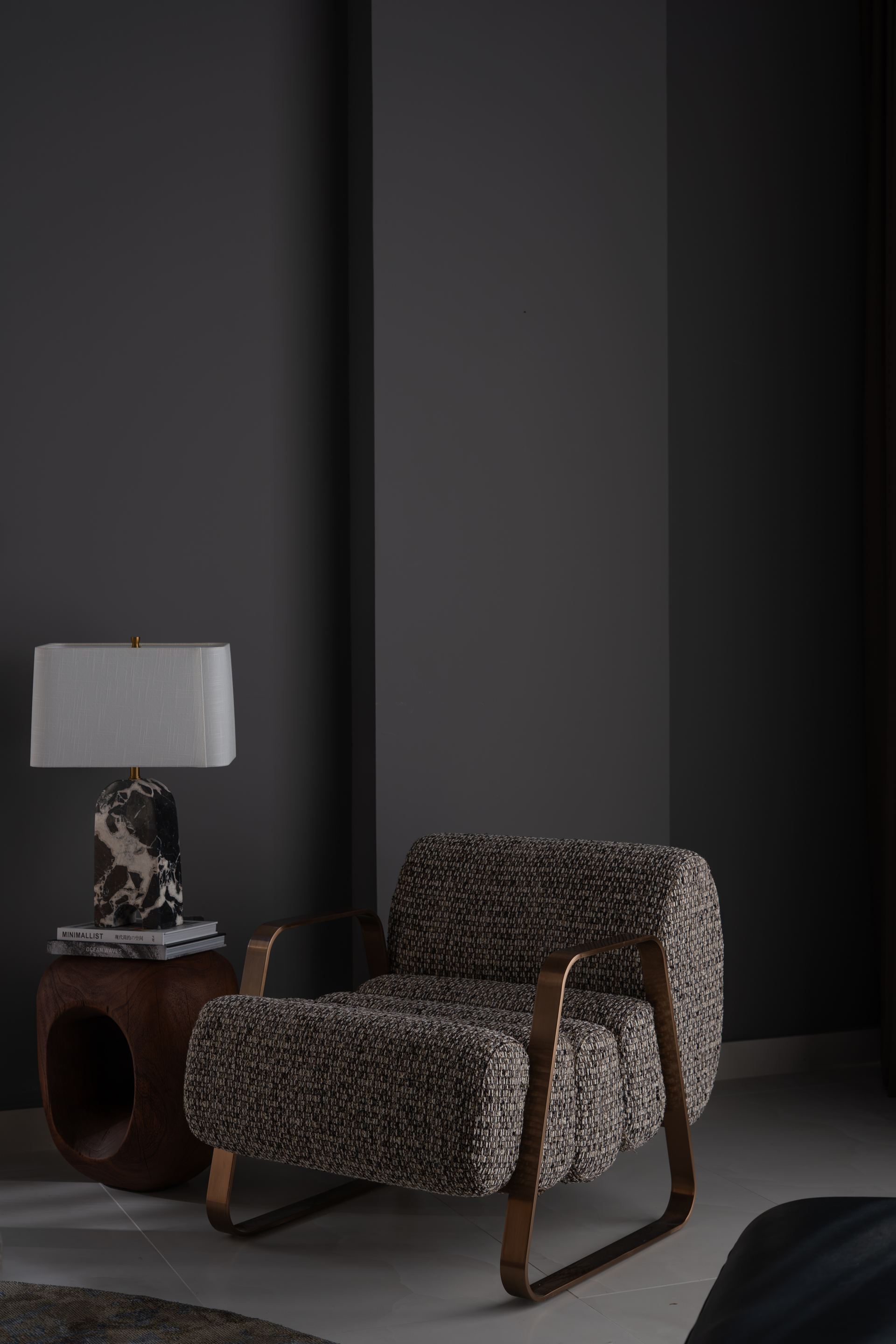 Bouclé armchair beside a marble-based table lamp in a dark room