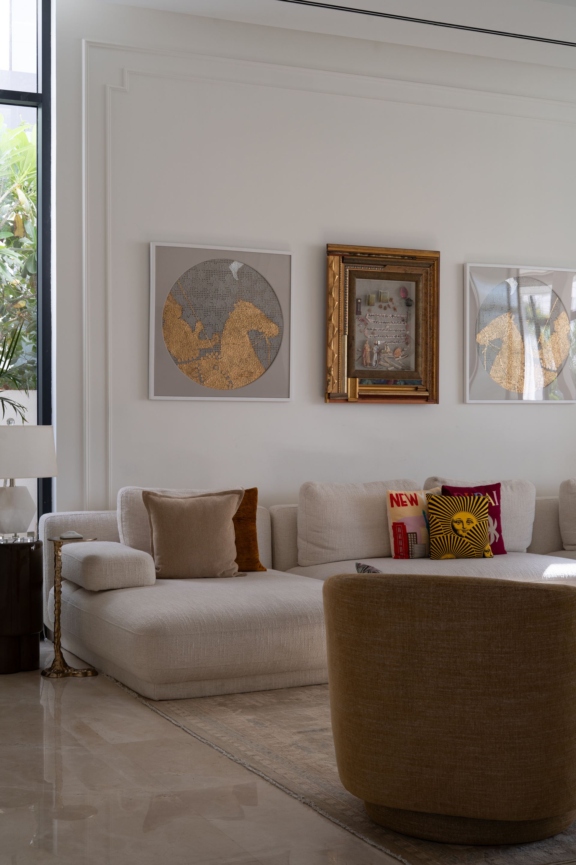 Round gold-leaf artworks flank a framed vintage print above a cream sectional
