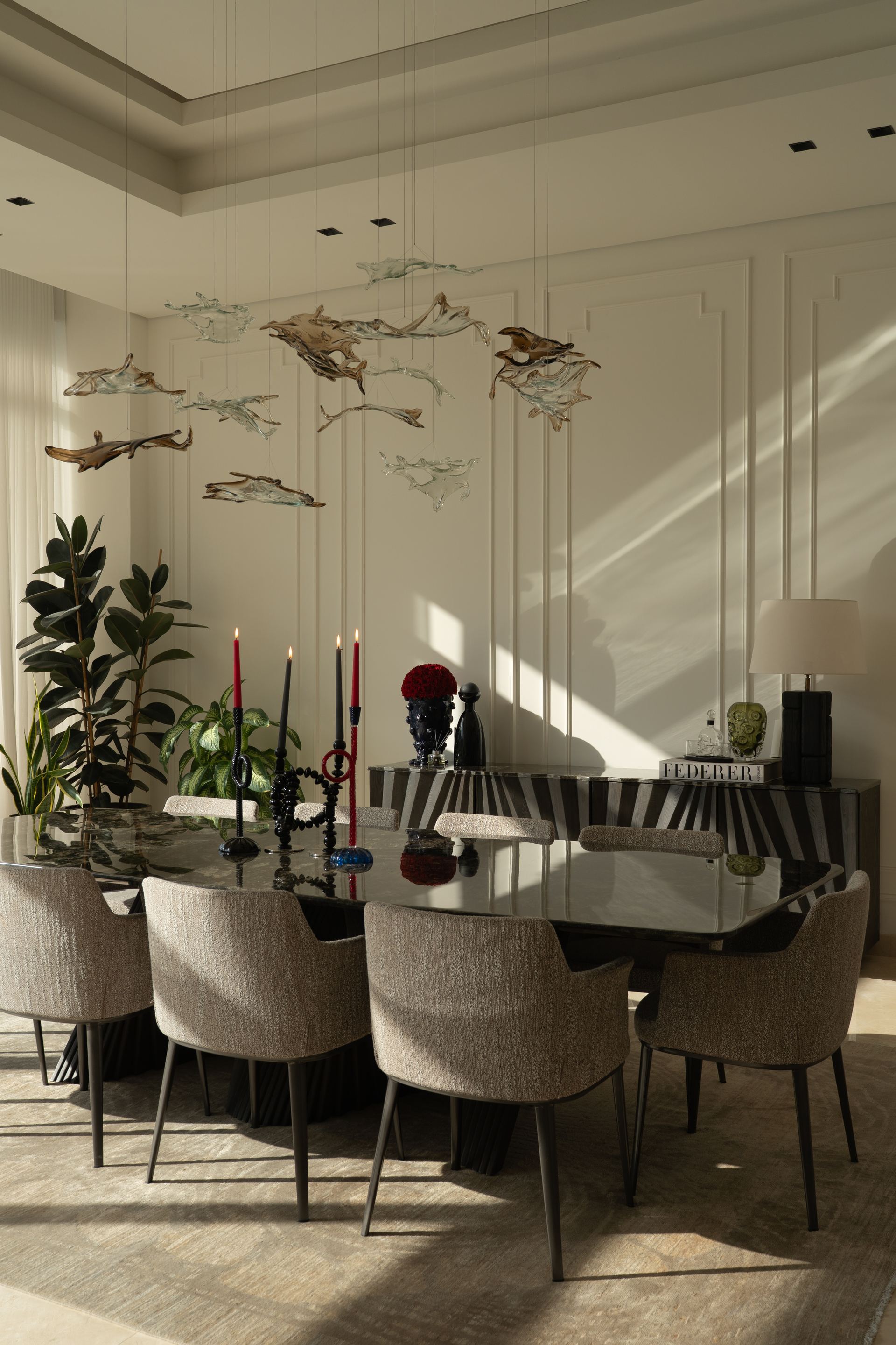 Dining table set with taper candles beneath a school of hand-crafted fish sculptures
