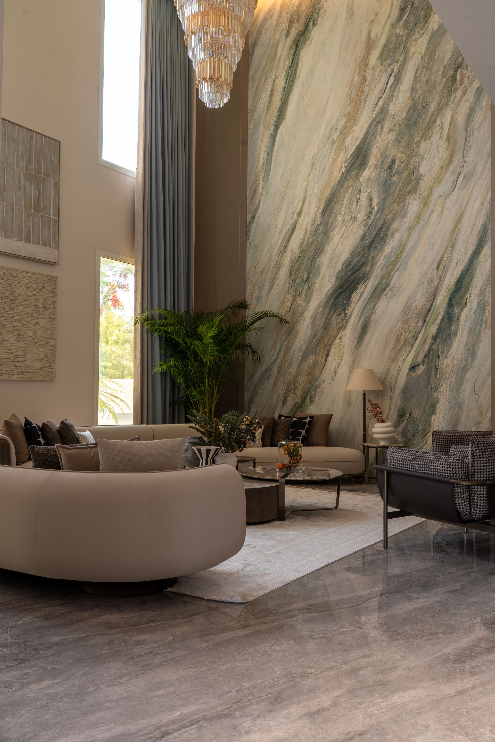 Curved bouclé sofa beneath a crystal chandelier against a striped green marble wall