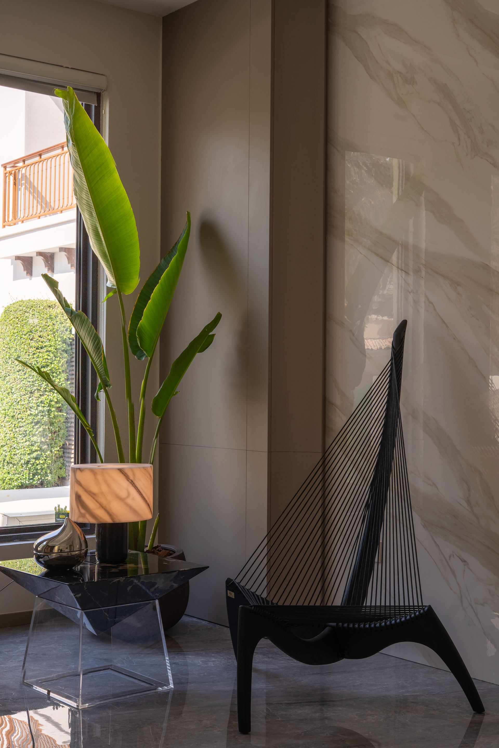 Sculptural black chair beside a bird-of-paradise plant against a marble-clad wall