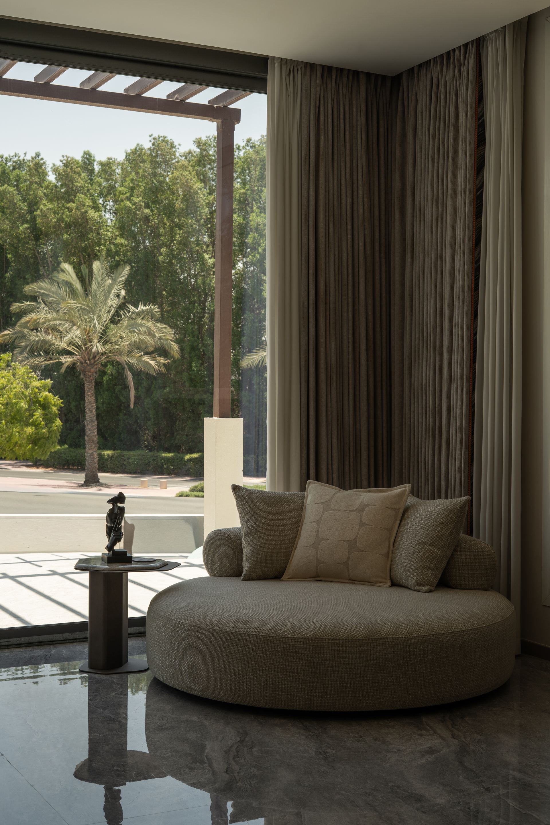 Round bouclé daybed beneath a wooden pergola overlooking a palm tree