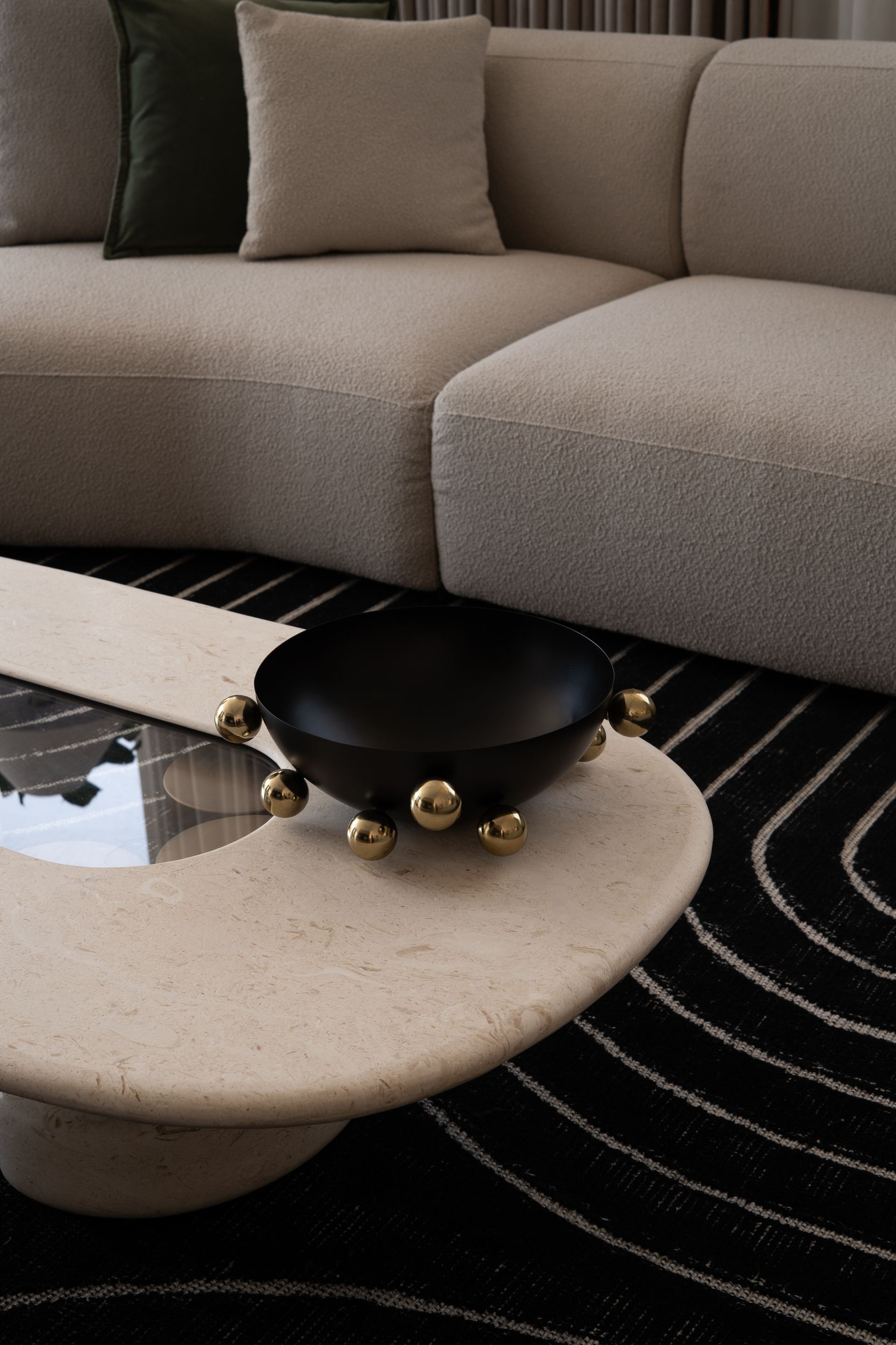 Black bowl with brass ball feet on a curved travertine coffee table