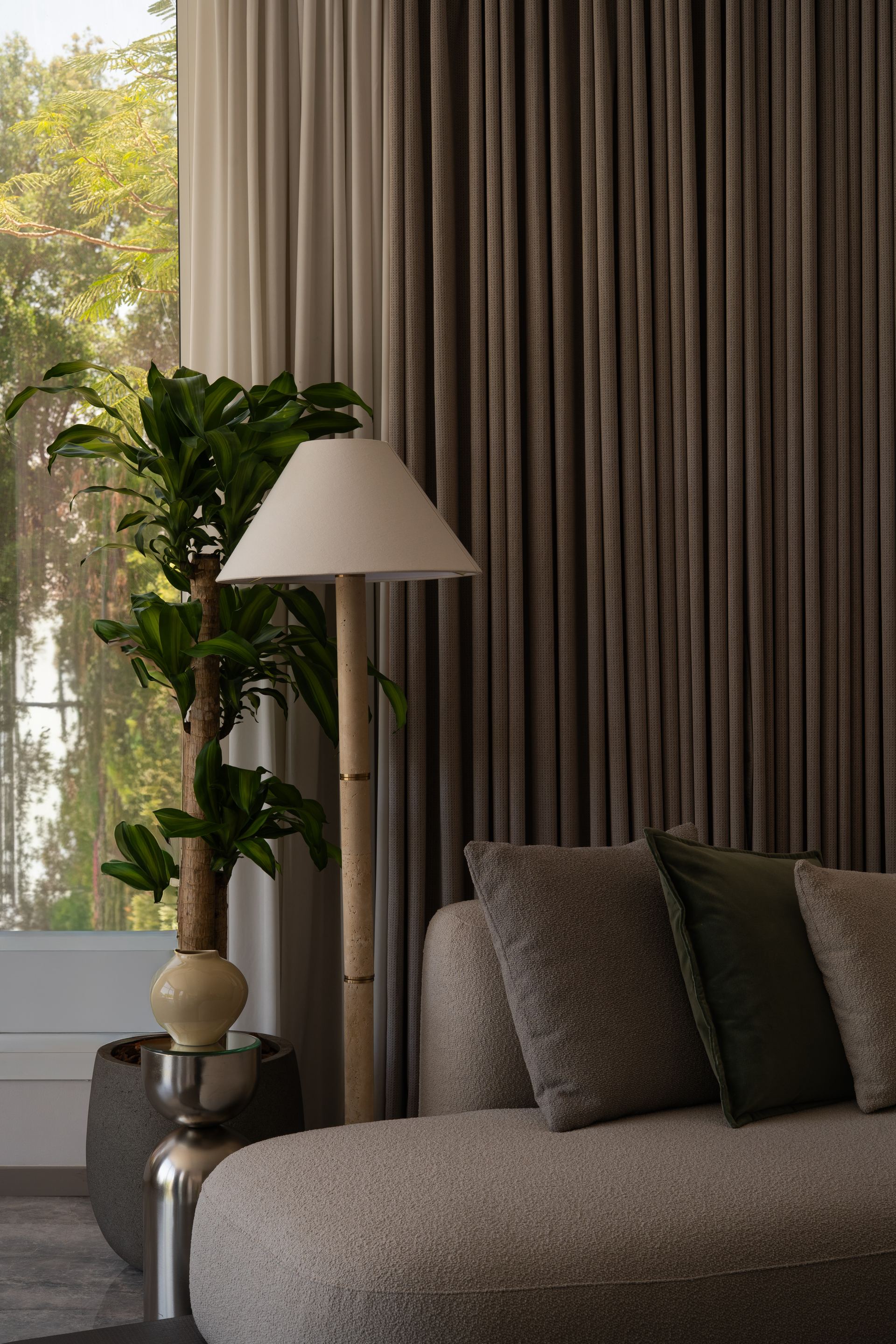 Wood floor lamp beside a potted dracaena against striped curtains