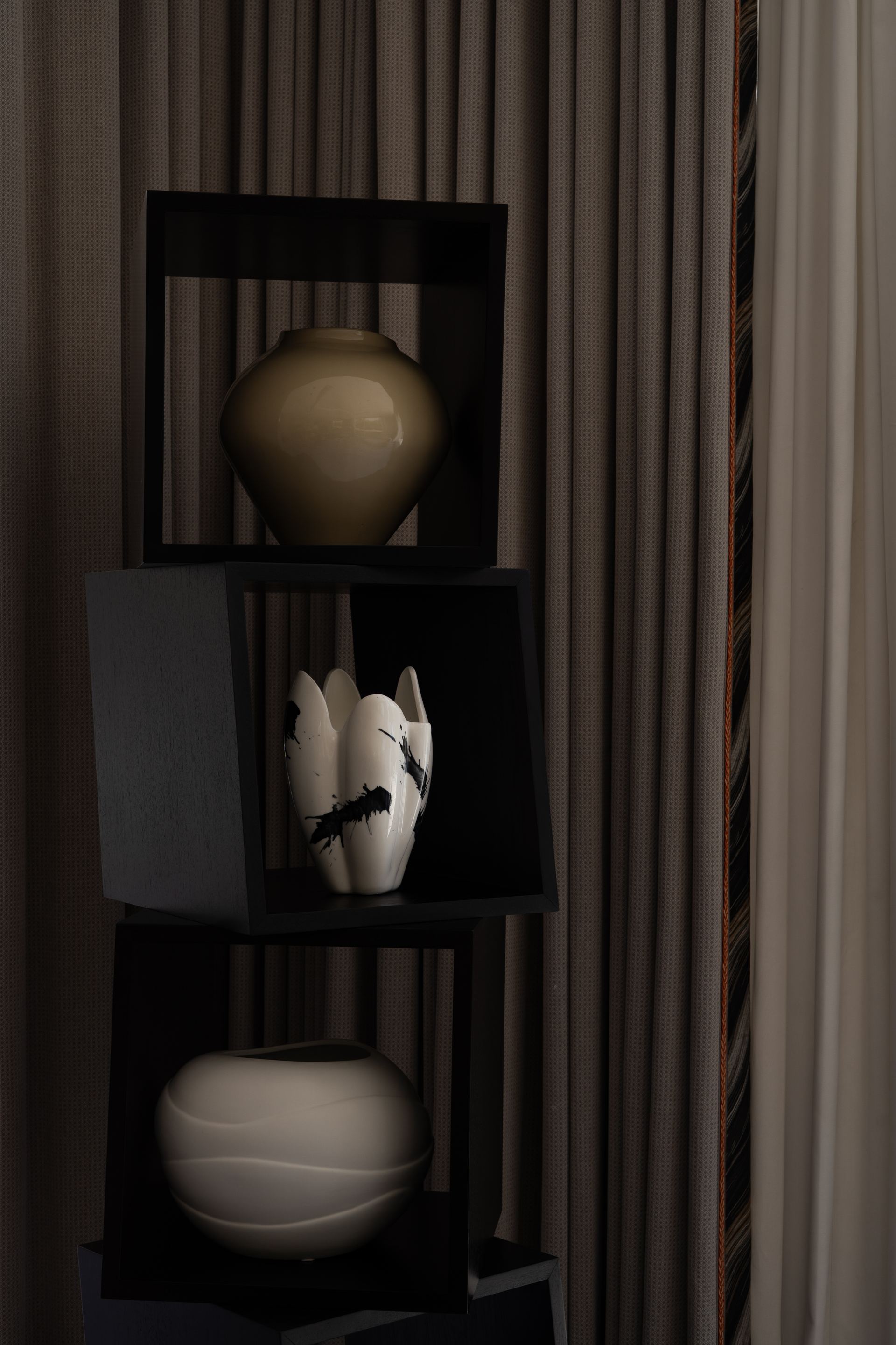 Ceramic vessels styled on a black display shelf against striped curtains