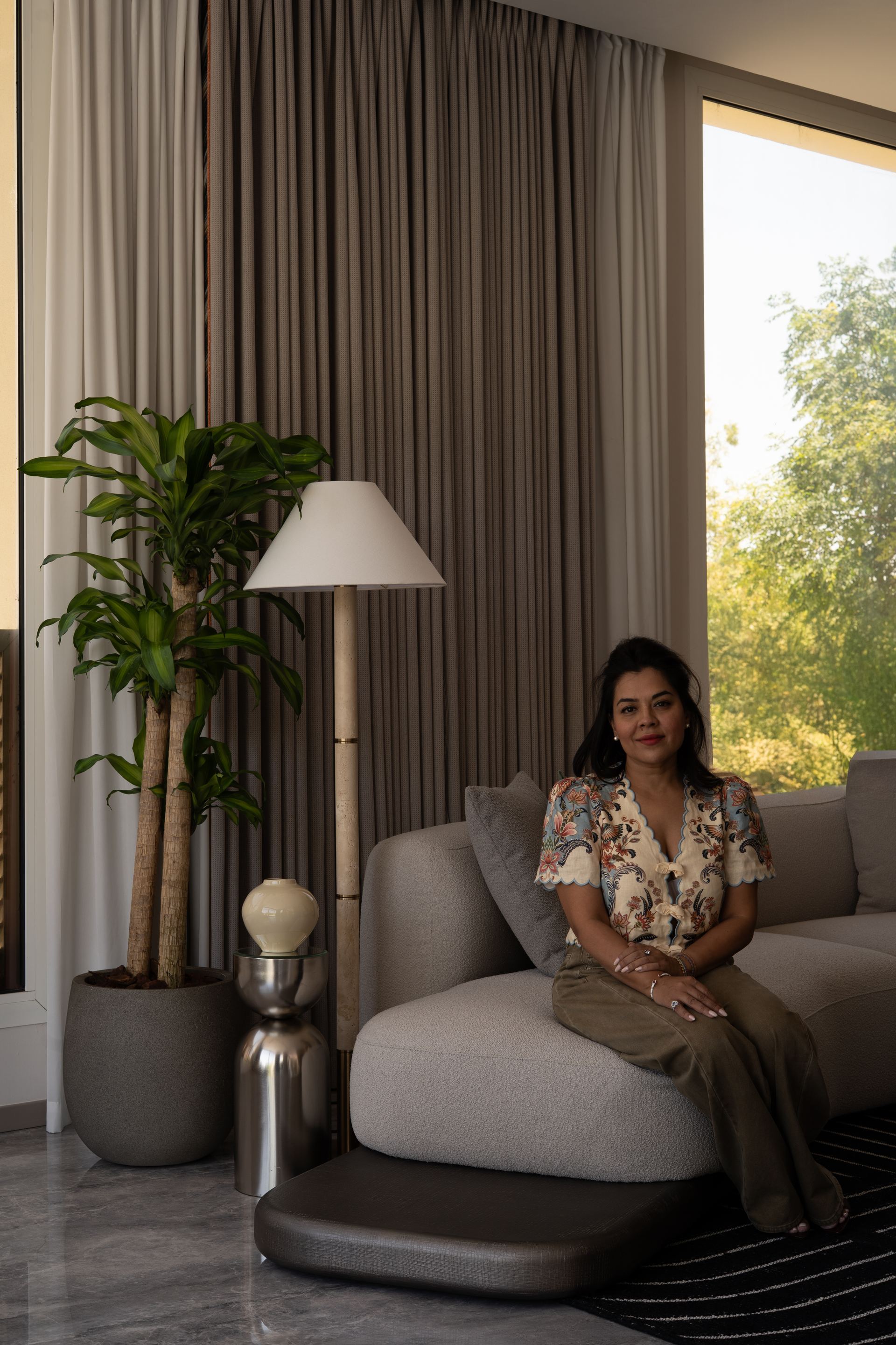 Floor lamp beside a potted plant and grey bouclé sofa by a garden-view window