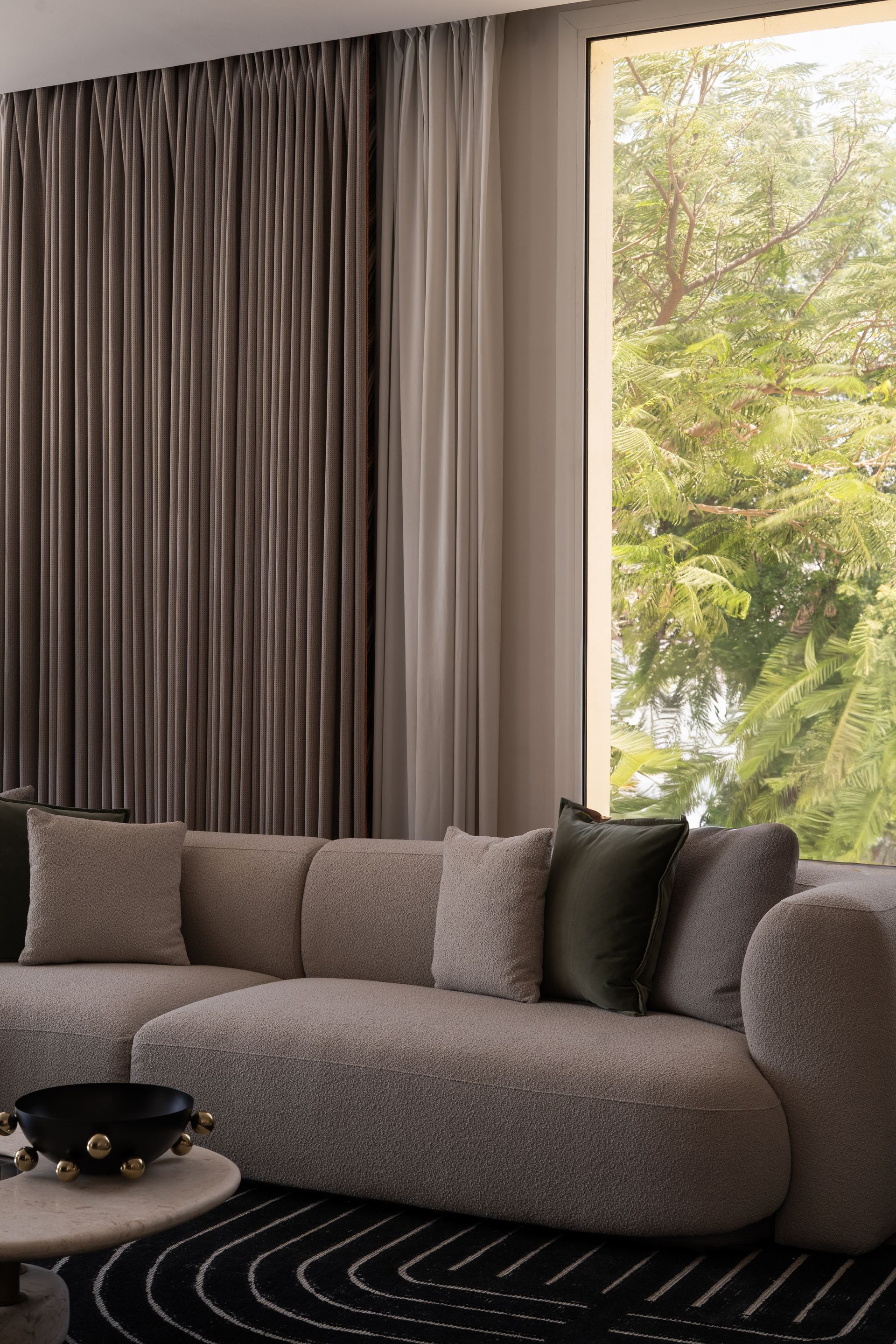 Grey sectional sofa with a striped rug and black bowl, framed by a tree-lined window