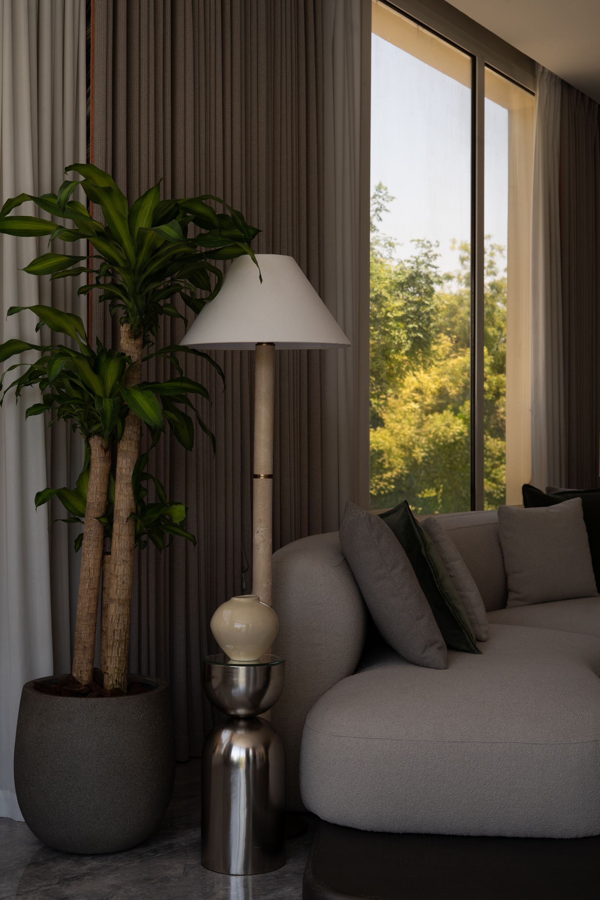 Potted dracaena beside a table lamp on a metal side table, next to a grey bouclé sofa