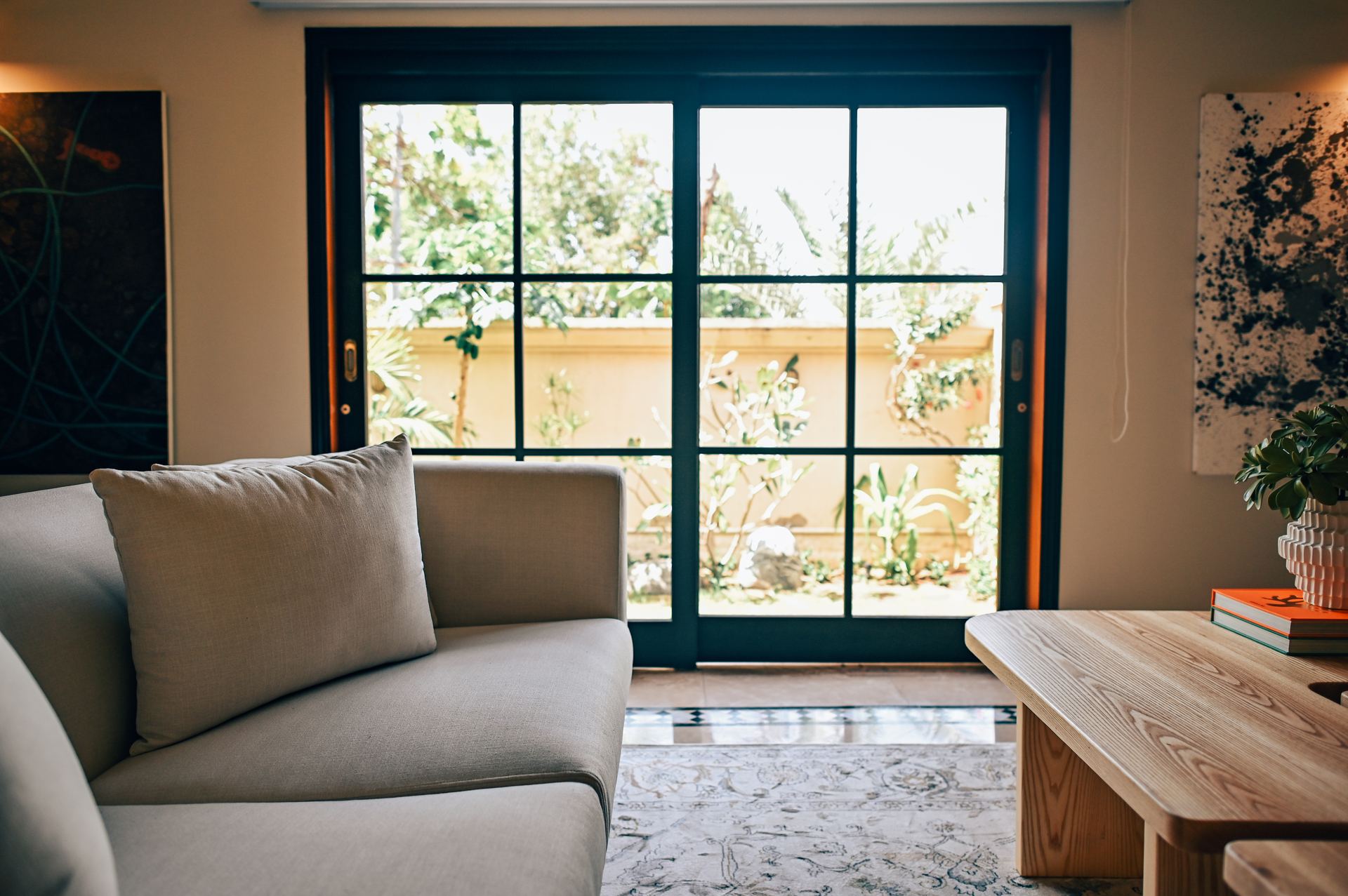 Garden view through black-framed French doors beside a linen sofa arm