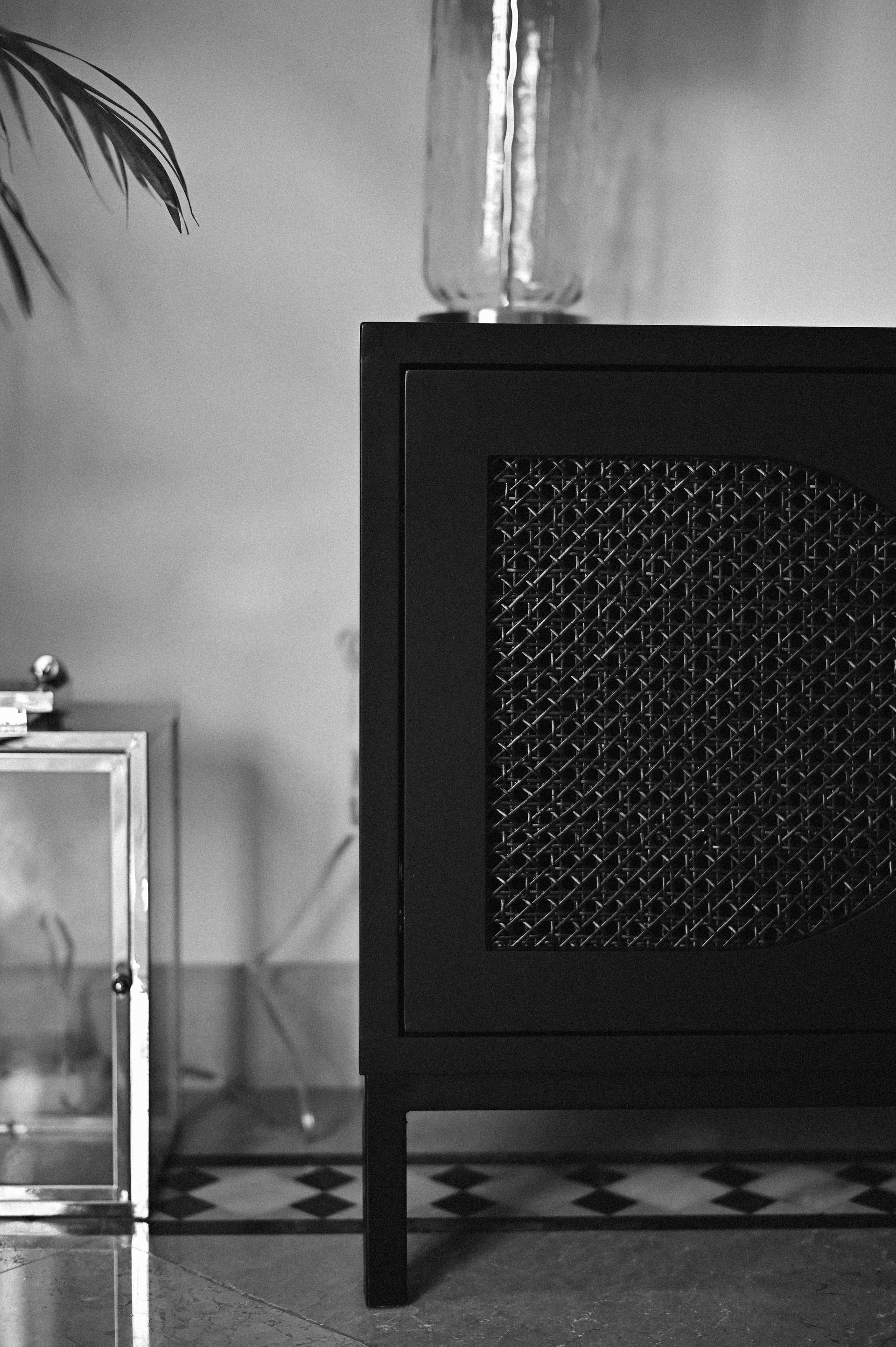 Black-and-white detail of a rattan-front black cabinet beside a glass lantern