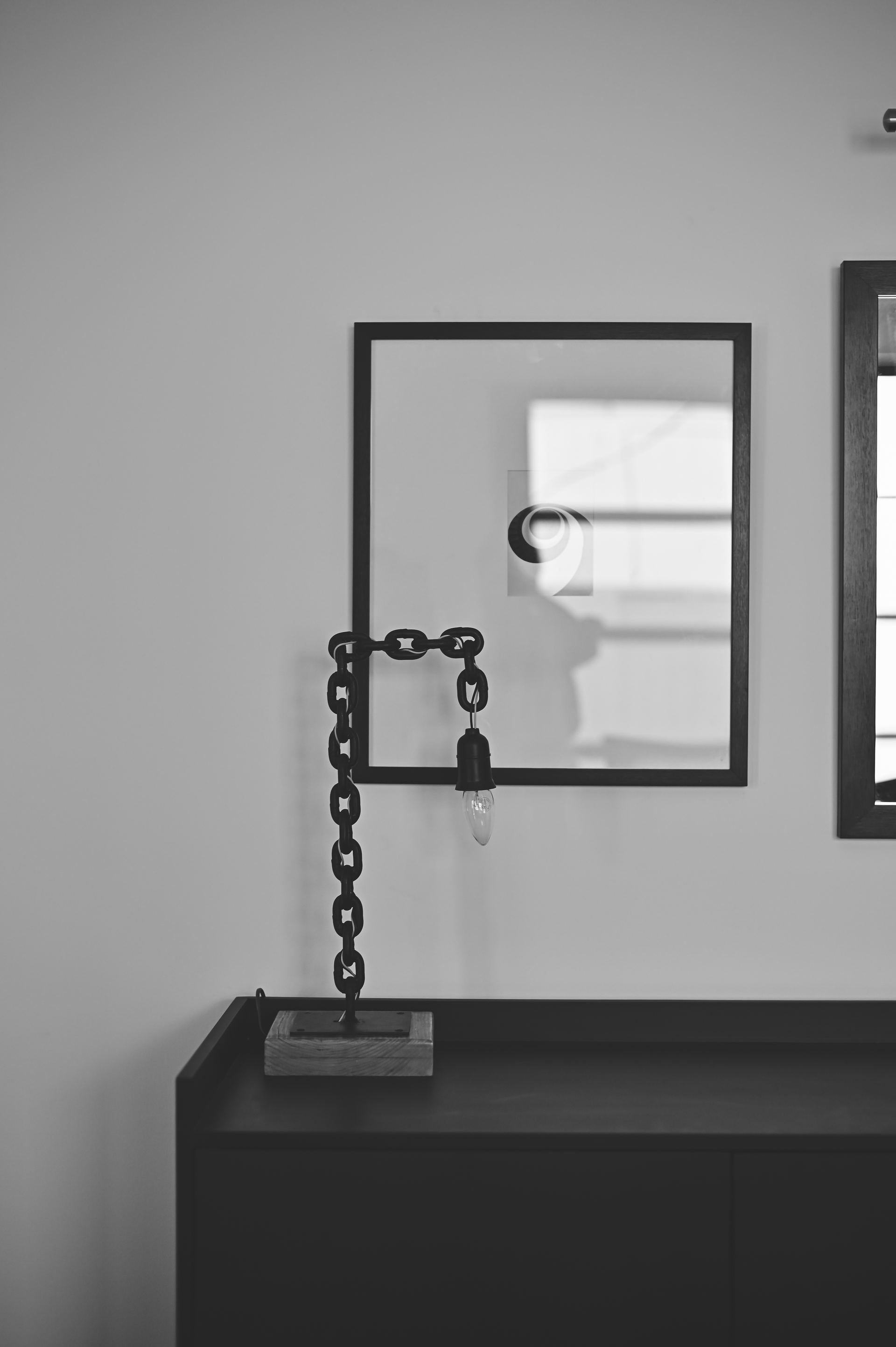 Sculptural chain wall light beside a mirror above a black console