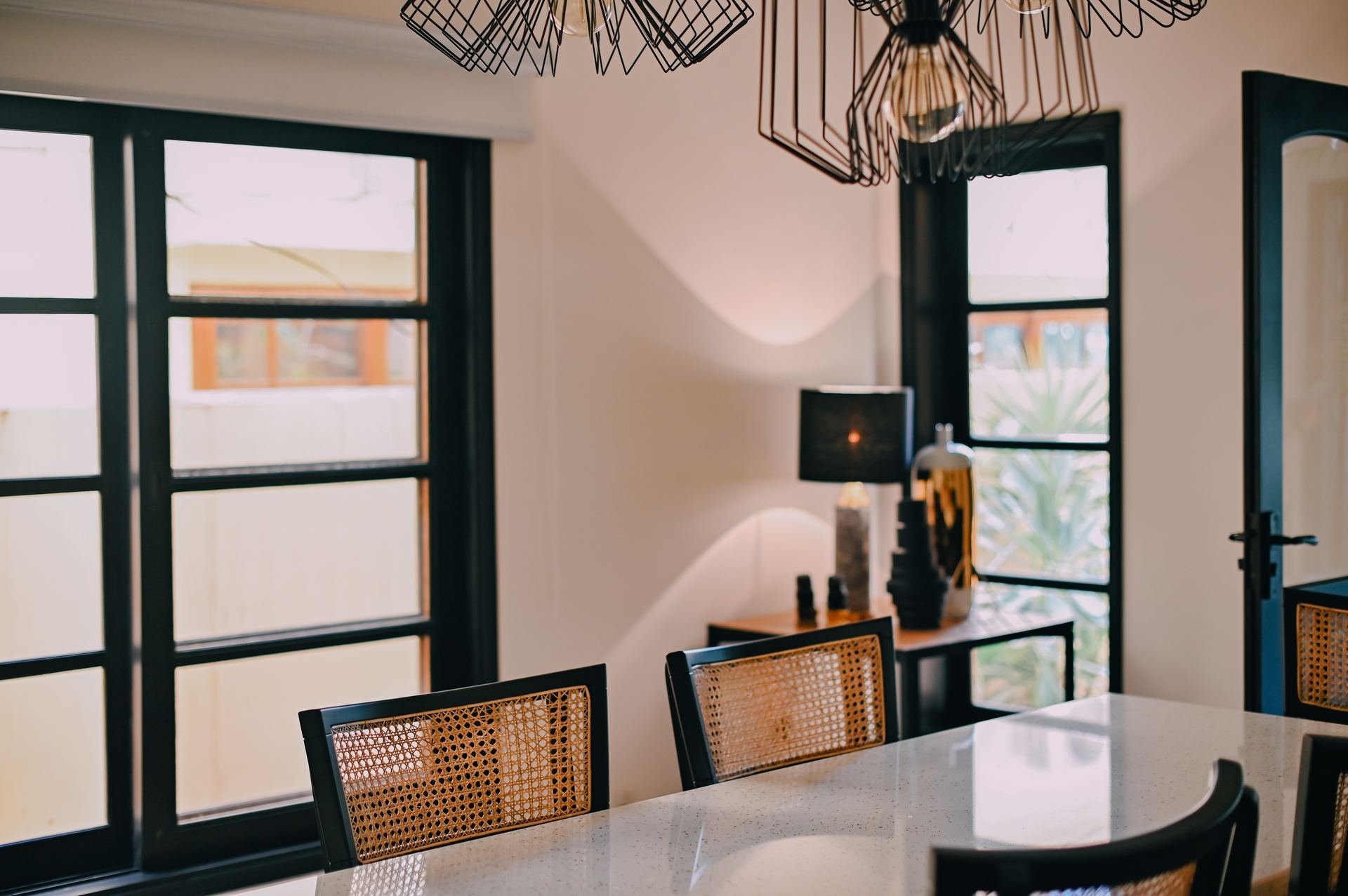 Wire-cage pendant lights above a marble dining table with cane chairs