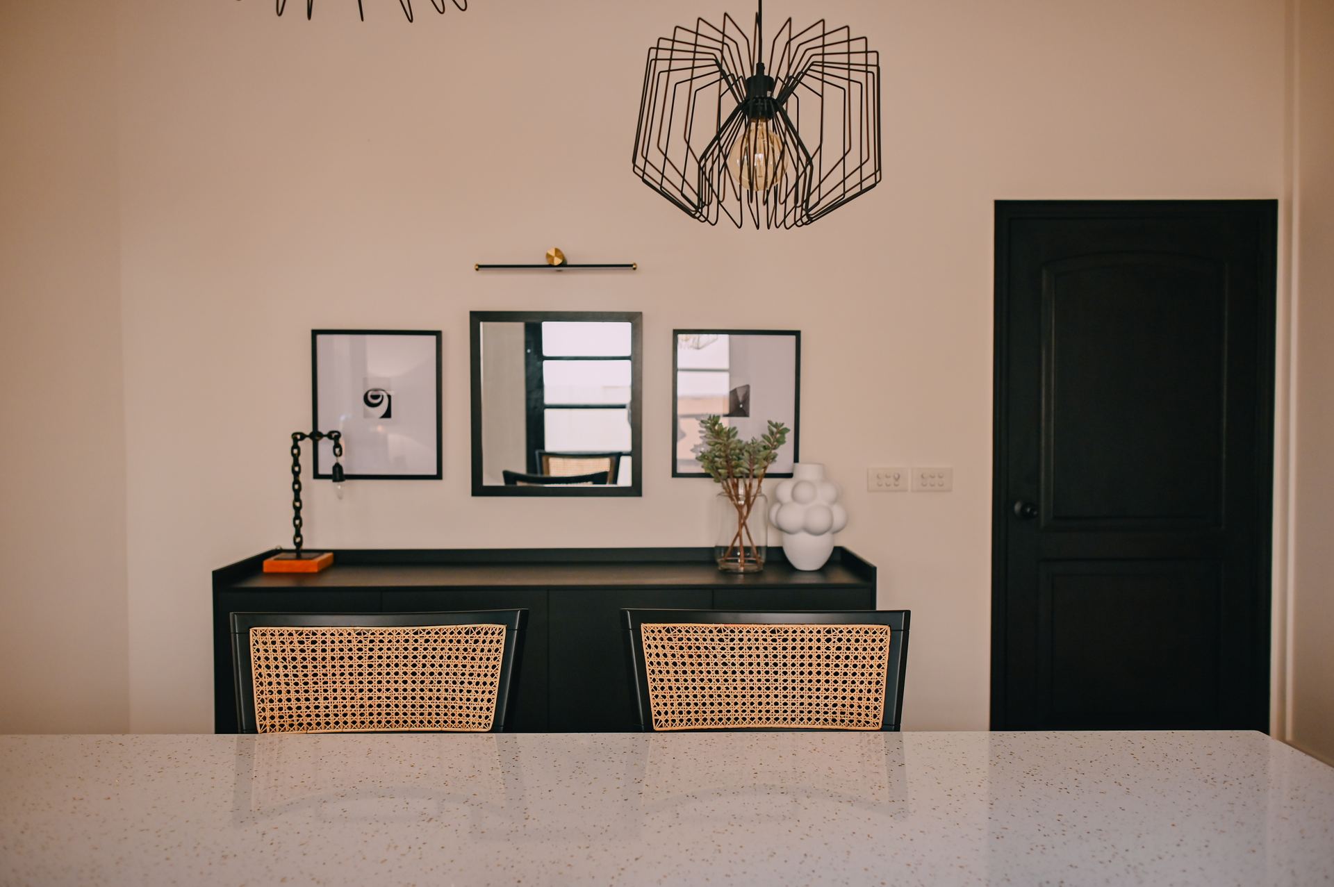 Cane-back dining chairs and a black console styled with framed art beneath a wire pendant light