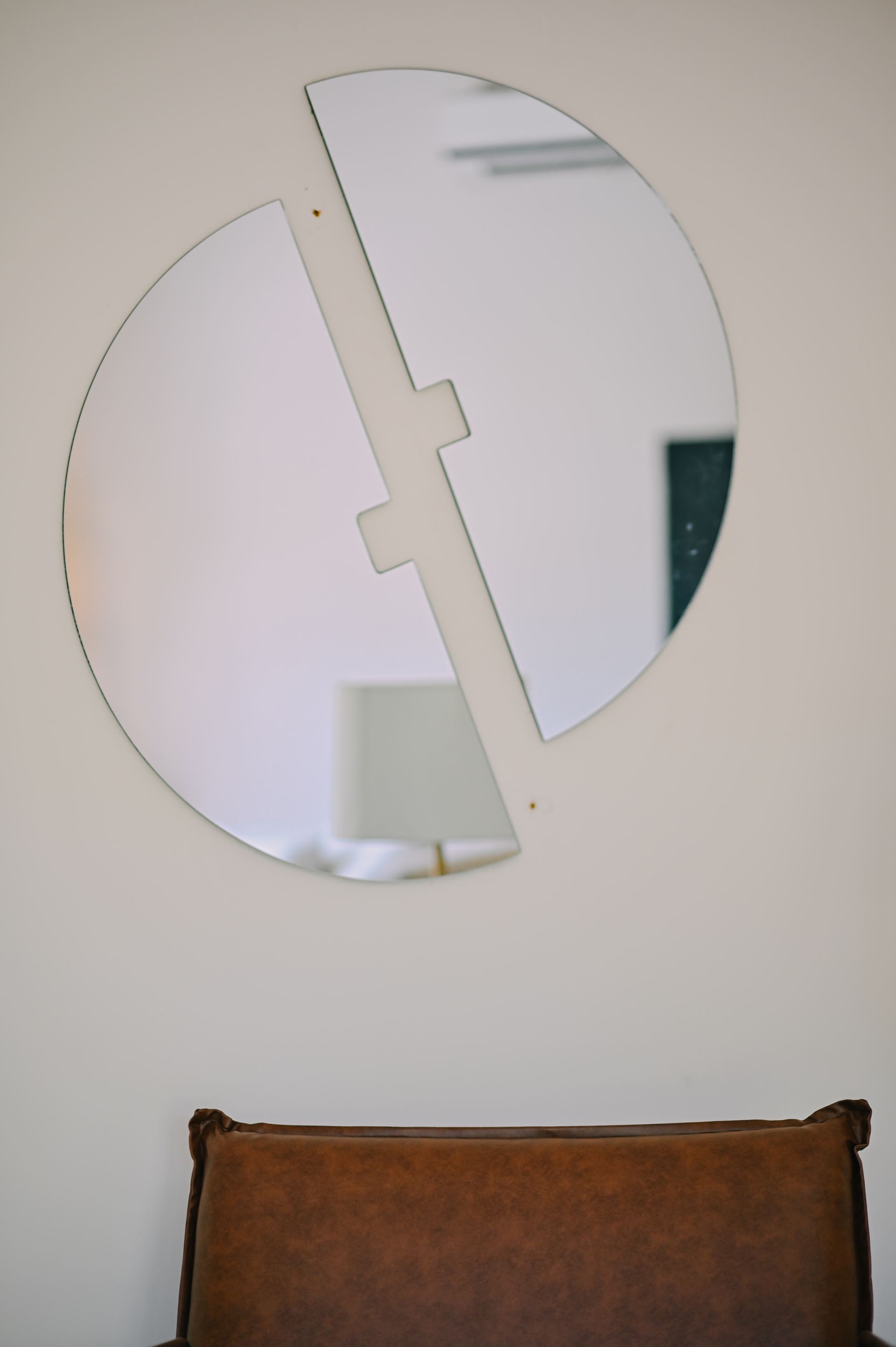 Black-and-white detail of a split circular mirror above a leather-backed chair