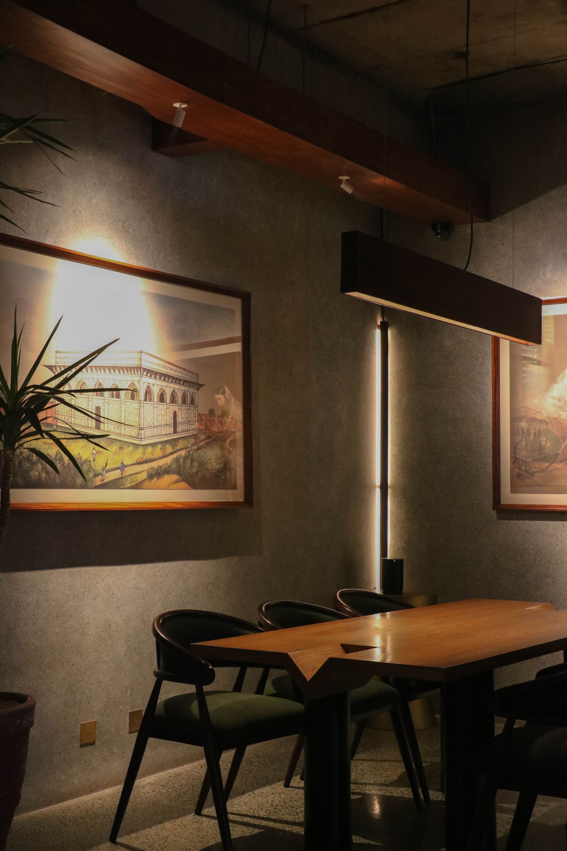 Green-upholstered dining chairs beneath a framed archival illustration and pendant light