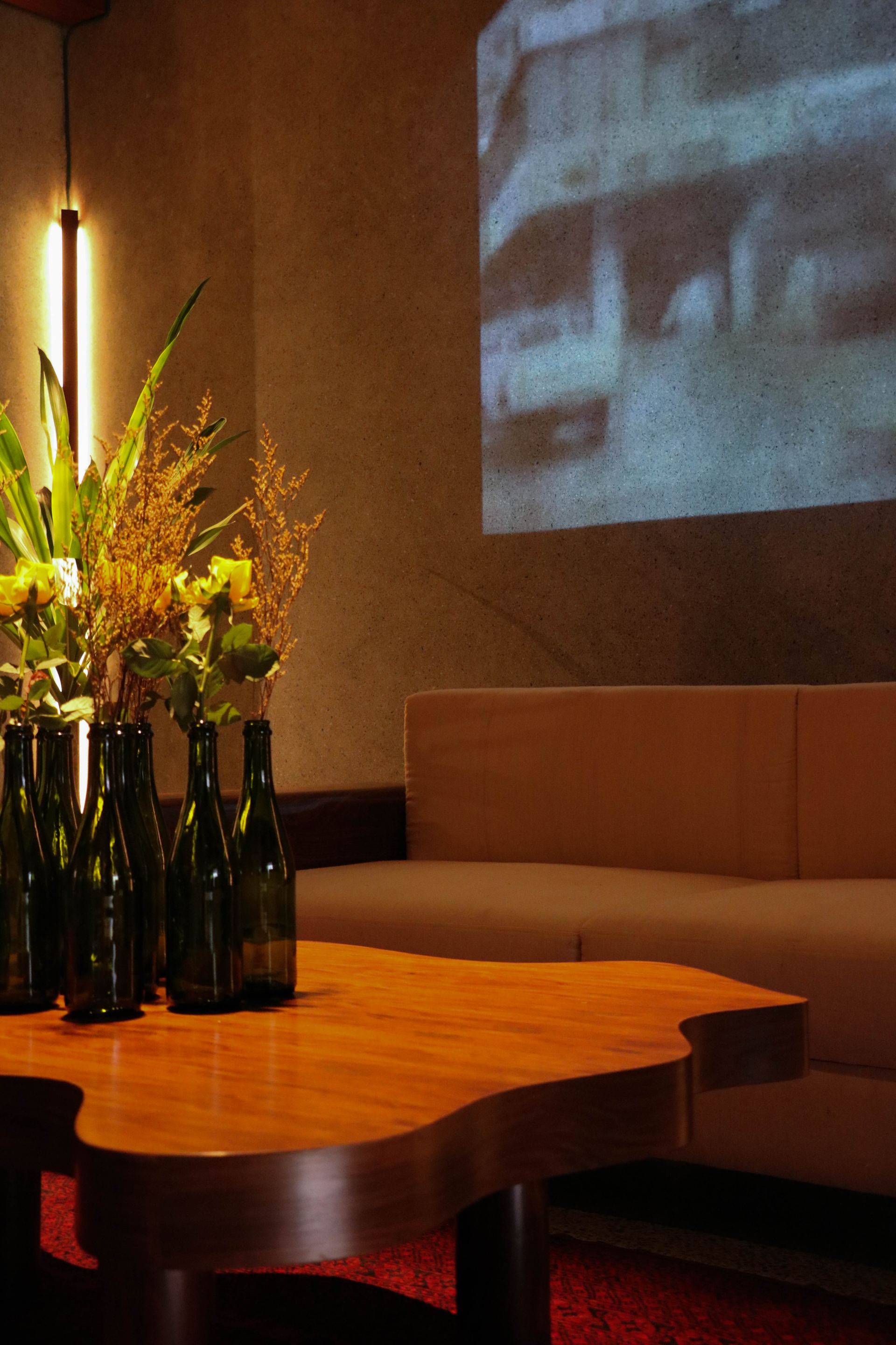 Green glass bottles of dried florals on a live-edge coffee table beneath a projected film