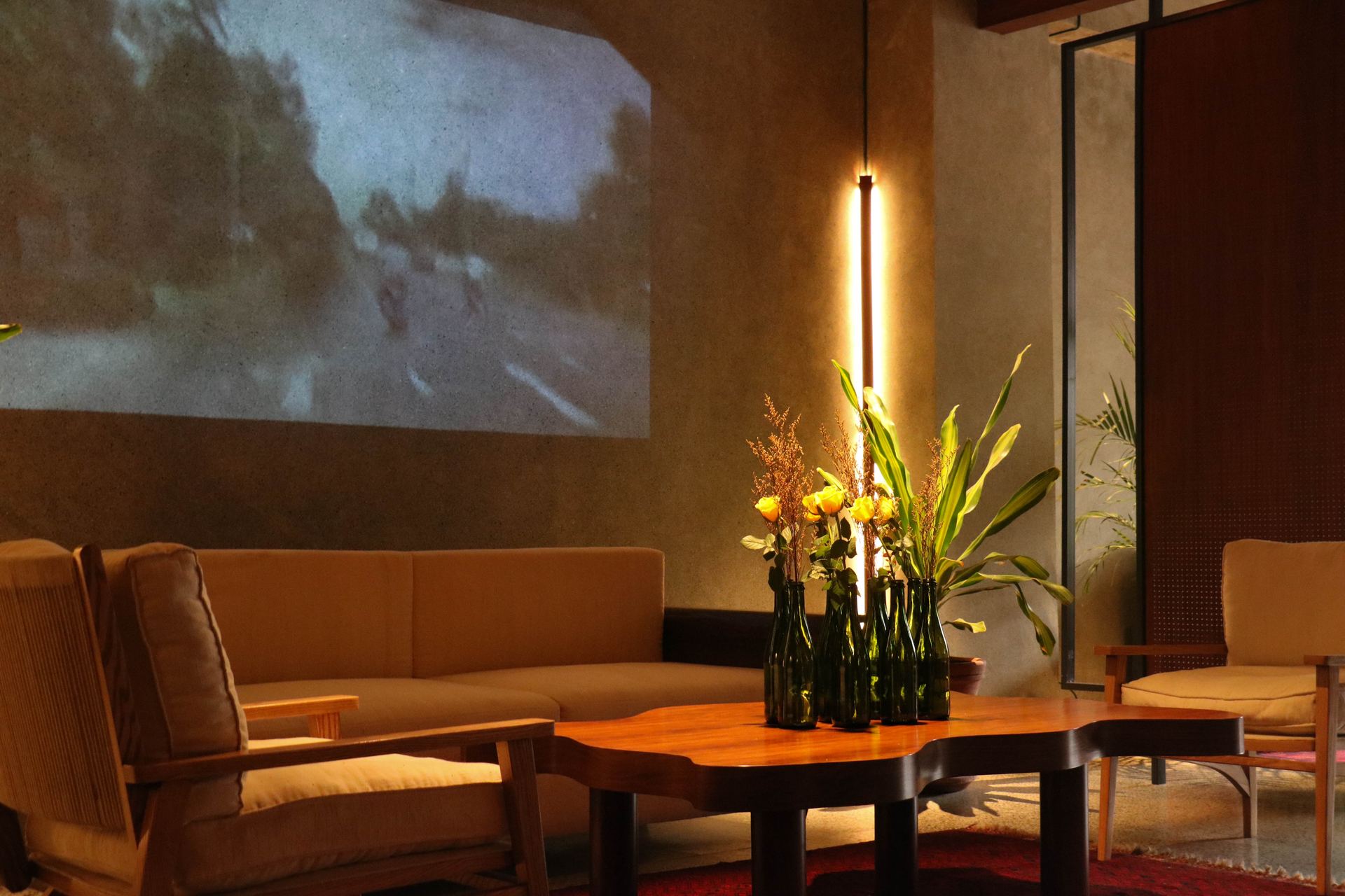 Green bottles of dried florals on a walnut coffee table beneath a projected vintage film